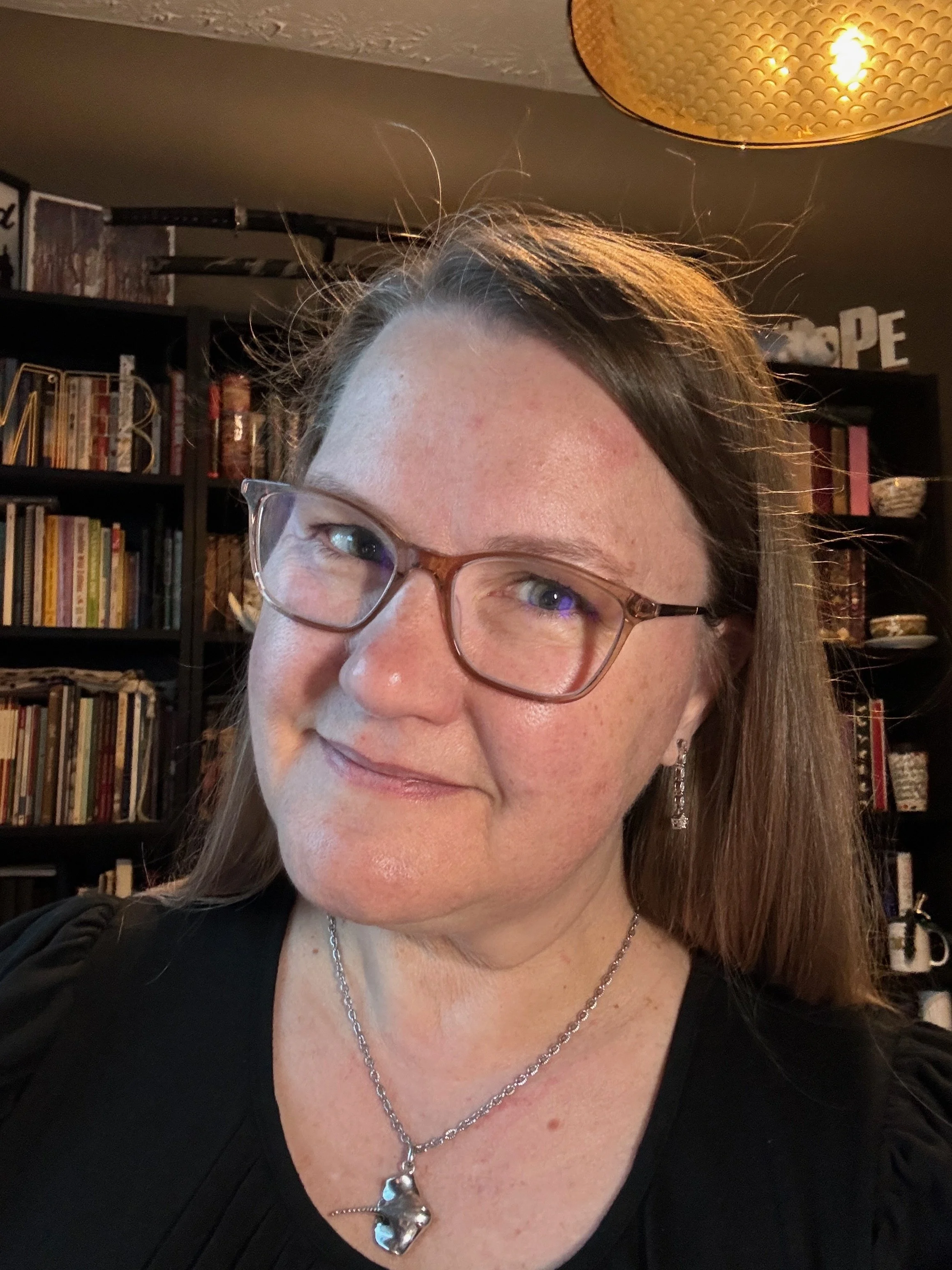 headshot of a woman smiling with glasses in front of a bookshelf full of books