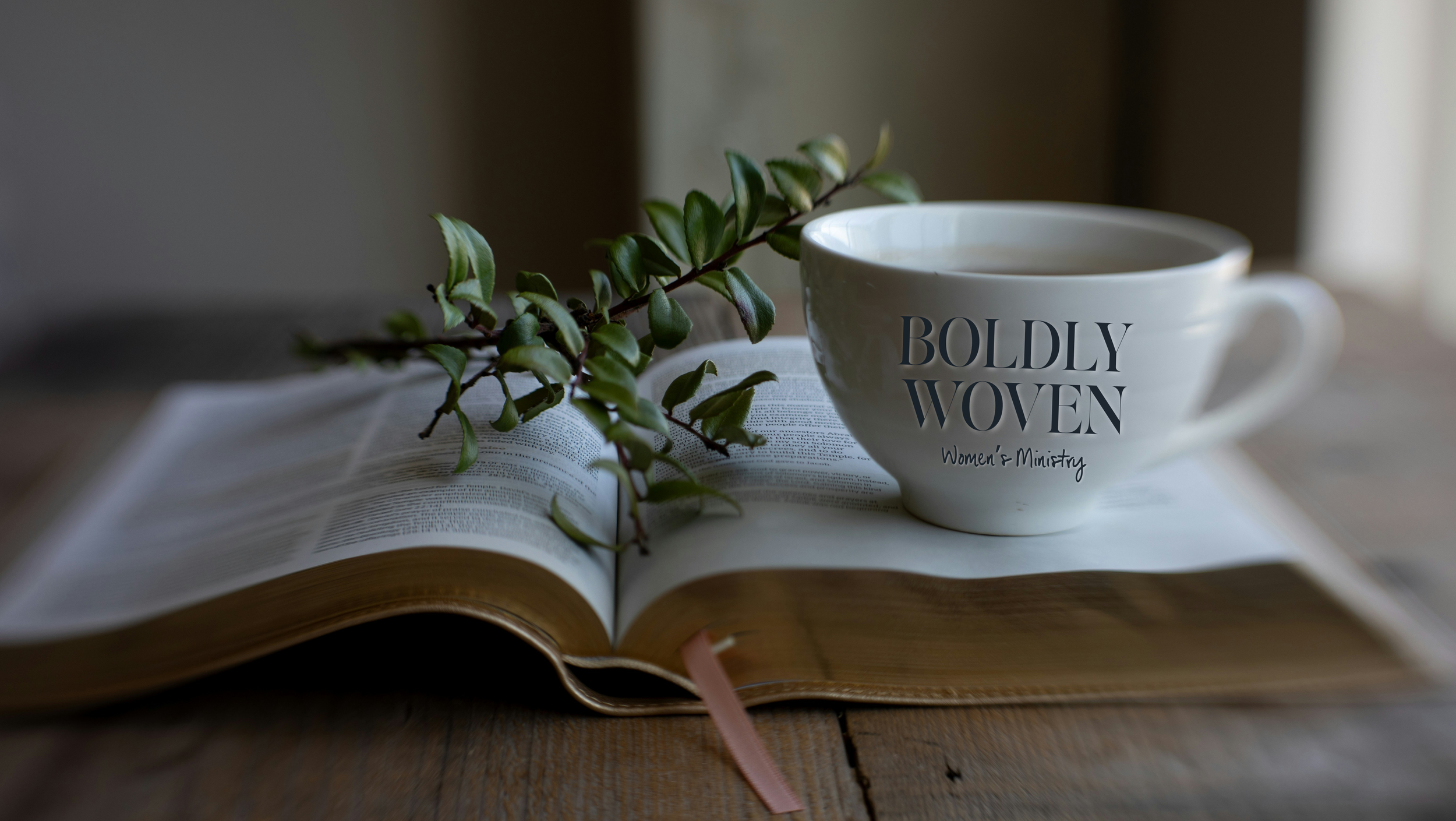 Bible with mug that says Boldly Woven Women's Ministry on it and greenery