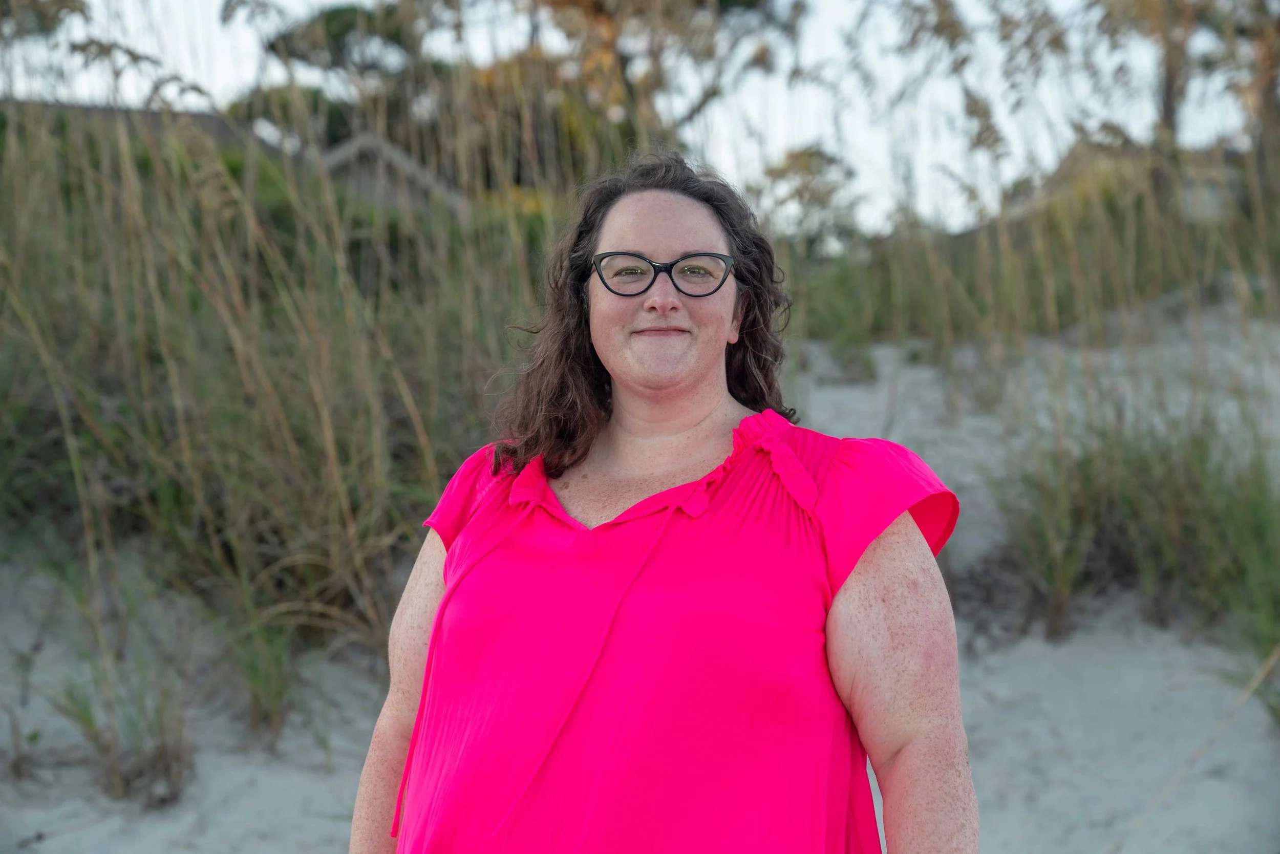 Woman standing on the beach smiling with dunes behind her