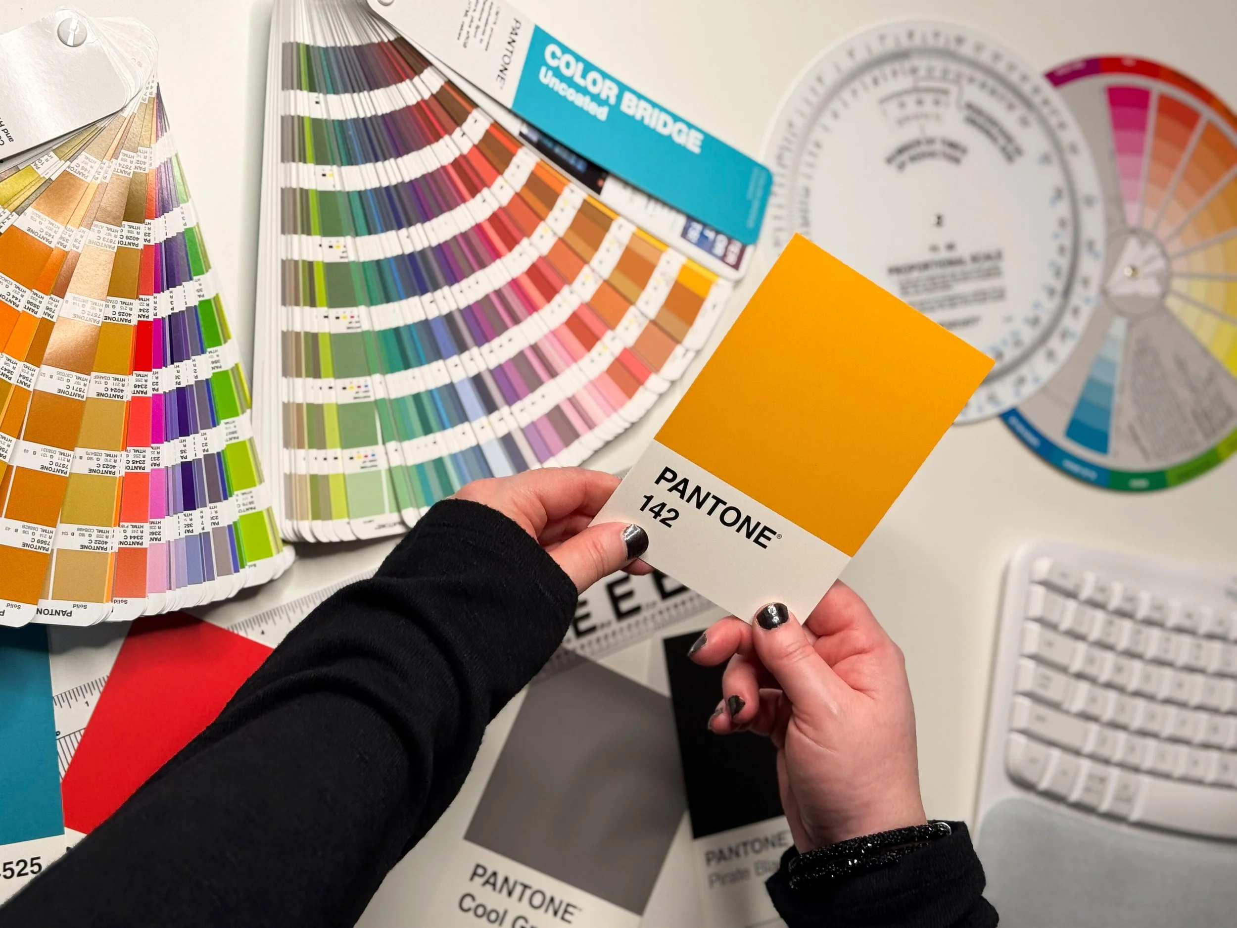 hands holding a pantone yellow swatch 142 with other swatches and graphic design tools around