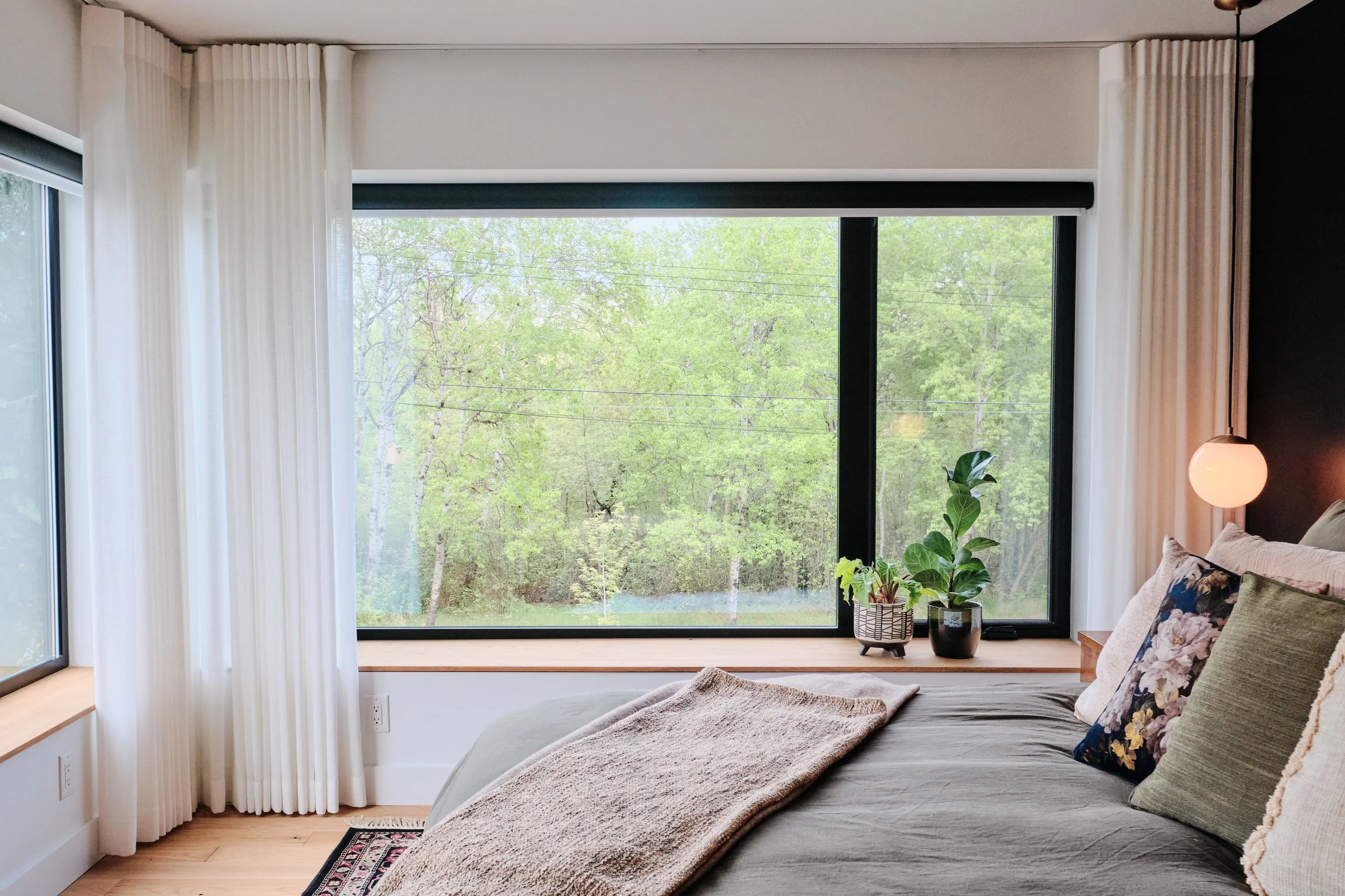 Stylish bedroom showcasing clean lines, natural textures, and panoramic window views of mature trees.
