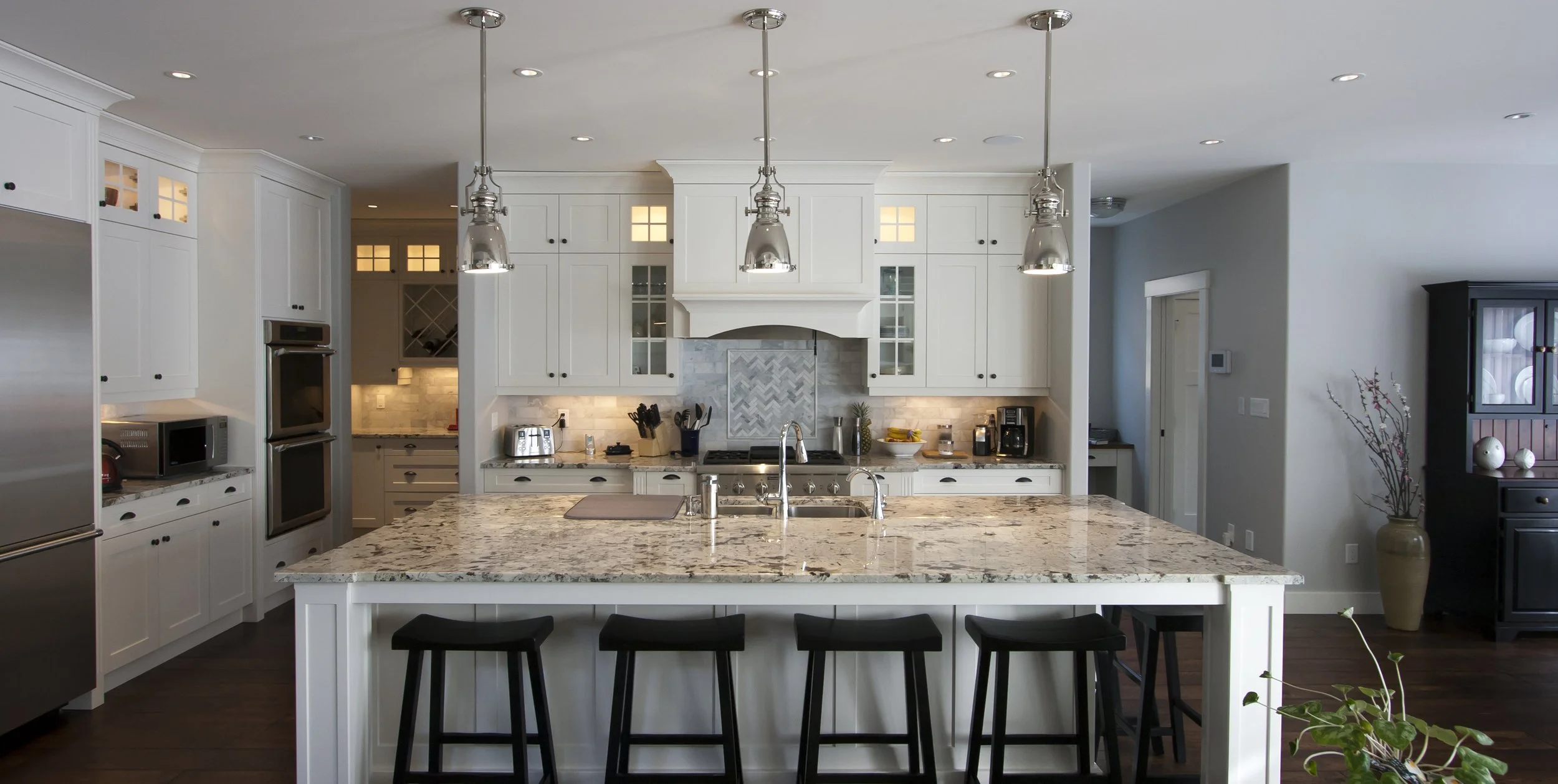 Modern kitchen with white cabinets, granite island, stainless steel appliances, and recessed lighting.