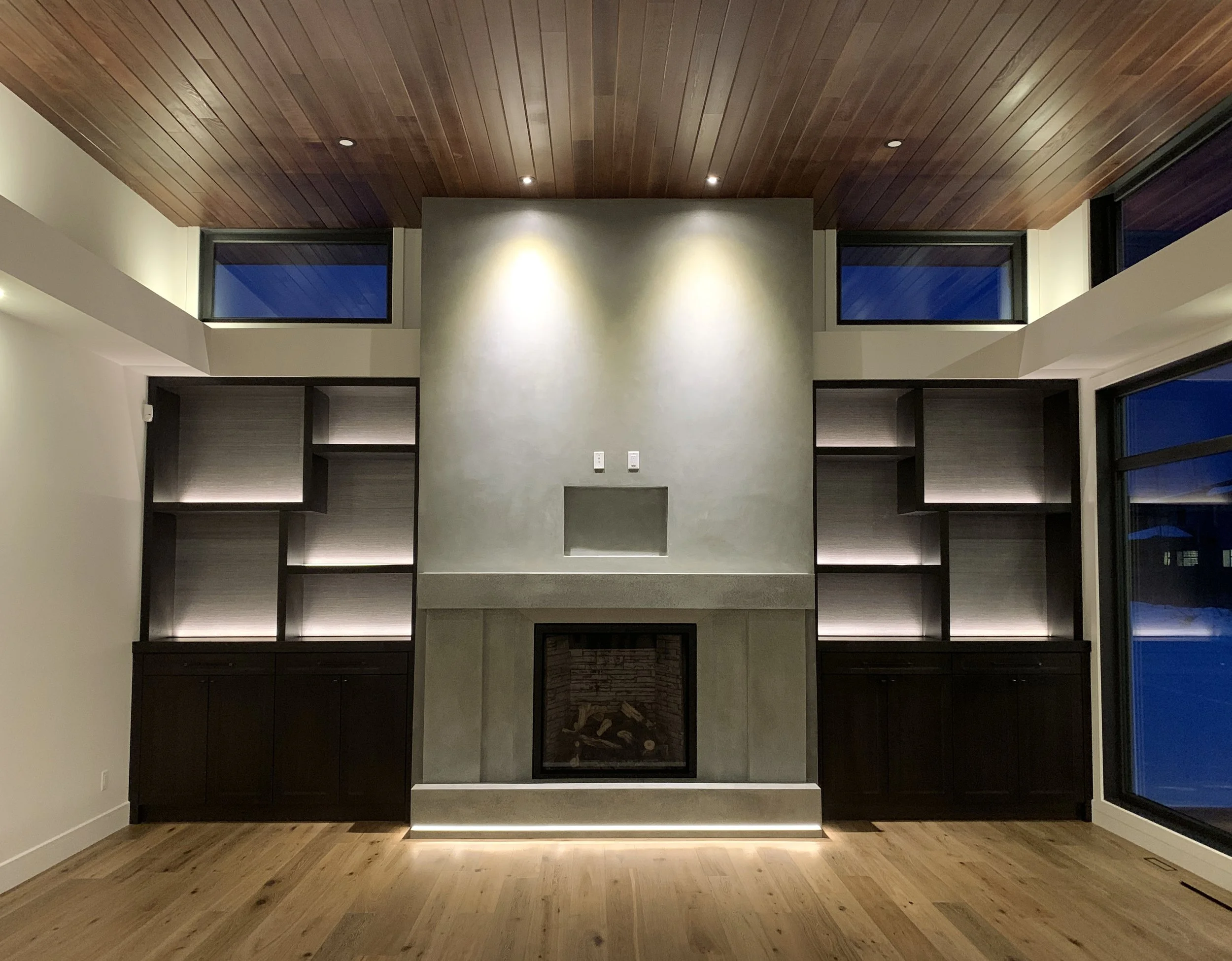 A living room with a concrete fireplace, custom cabinets and wood ceiling