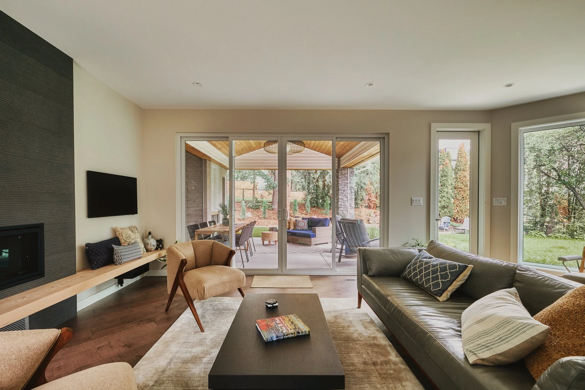 Living room with large sliding glass doors opening to a covered patio with outdoor seating and view of backyard with trees.