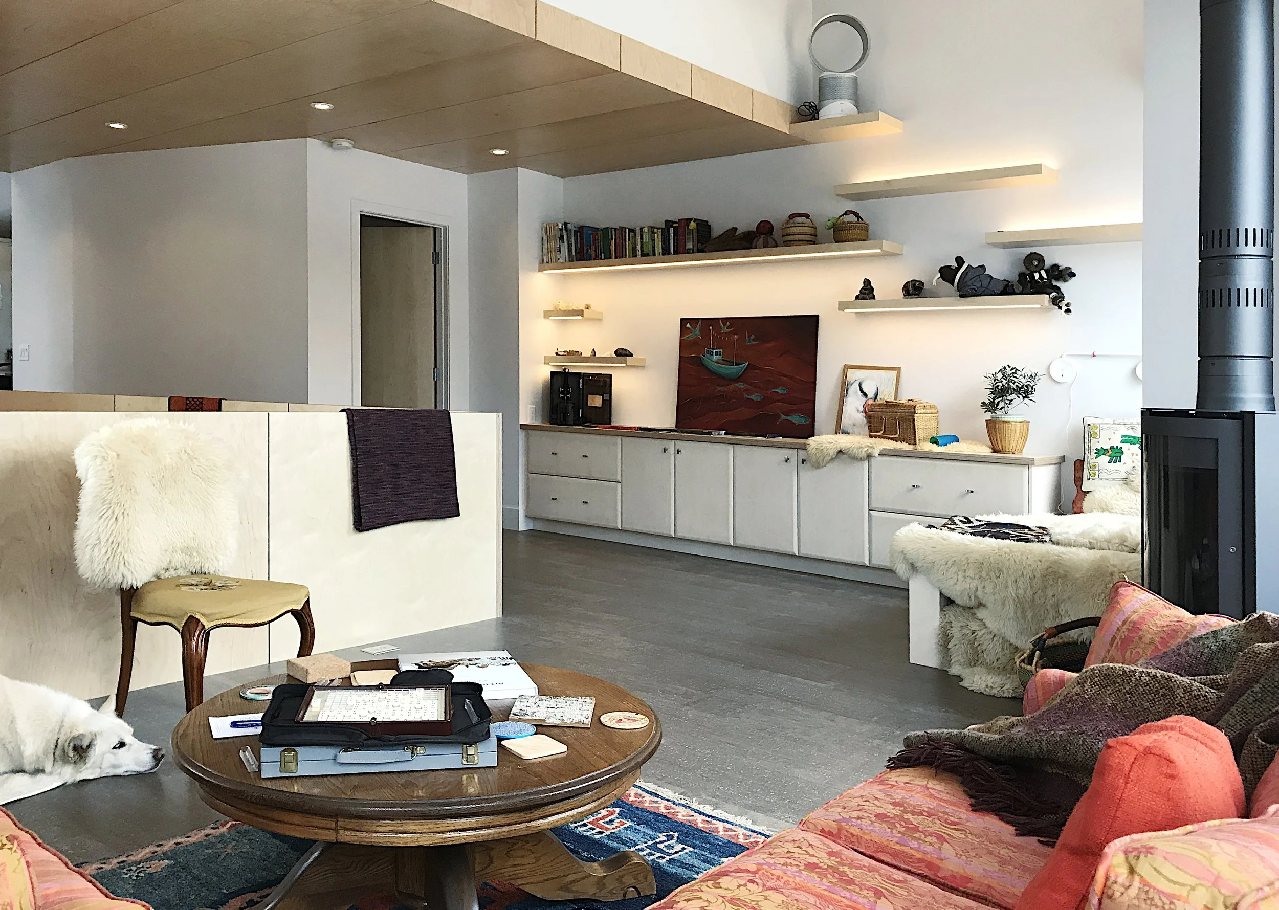 Modern cozy living space with light wood cabinetry, black wood-burning stove, illuminated shelves, rustic decor, and minimalist design—ideal for warm, stylish interiors blending modern and natural elements.