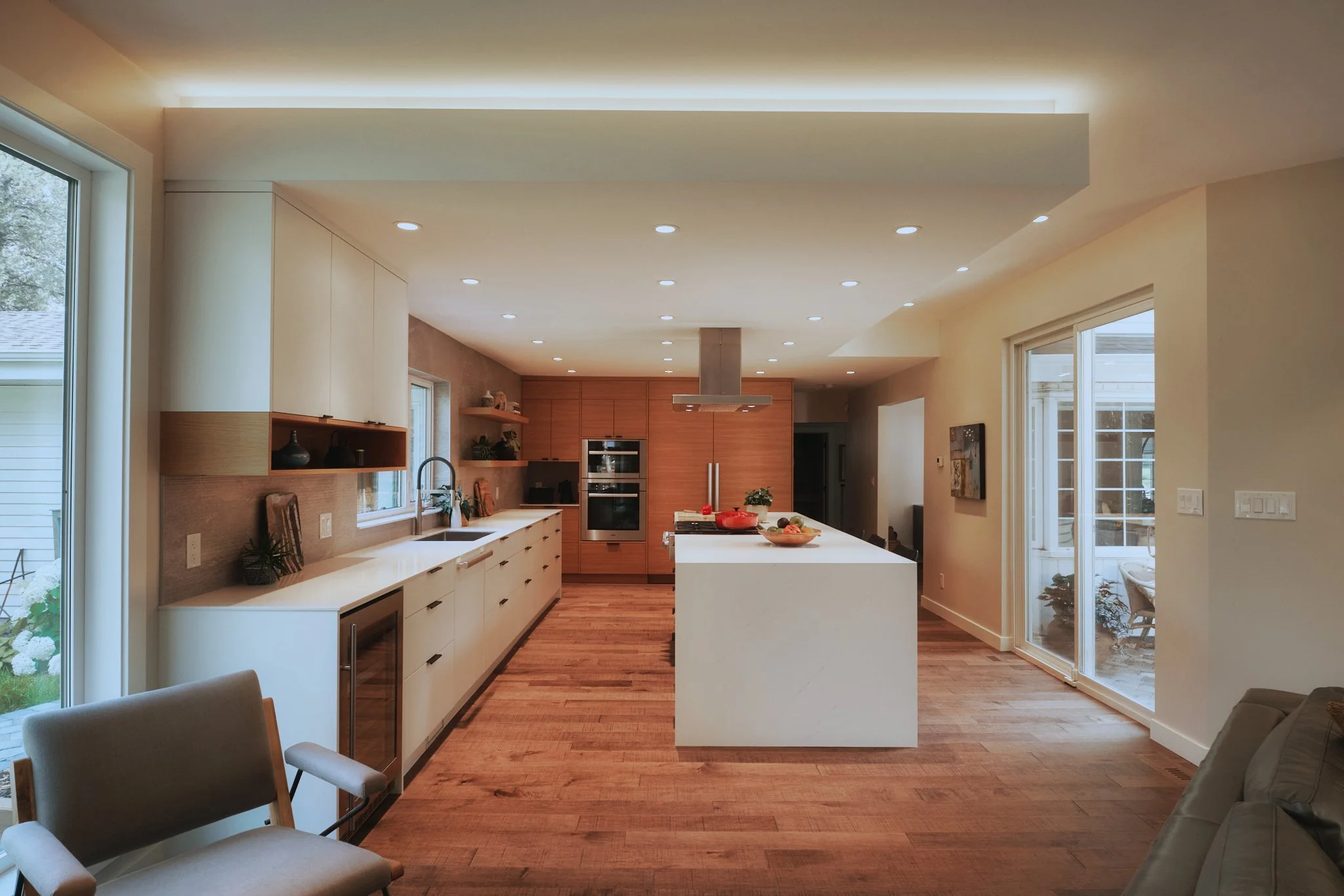 Modern kitchen with white island, wooden cabinets, stainless steel oven, and sliding glass door leading outside.