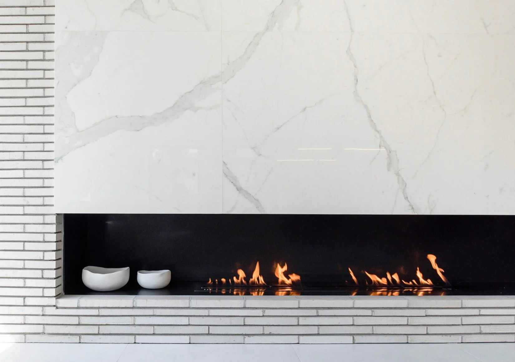 Modern linear fireplace with marble wall surround, minimalist design, and clean white brick hearth.