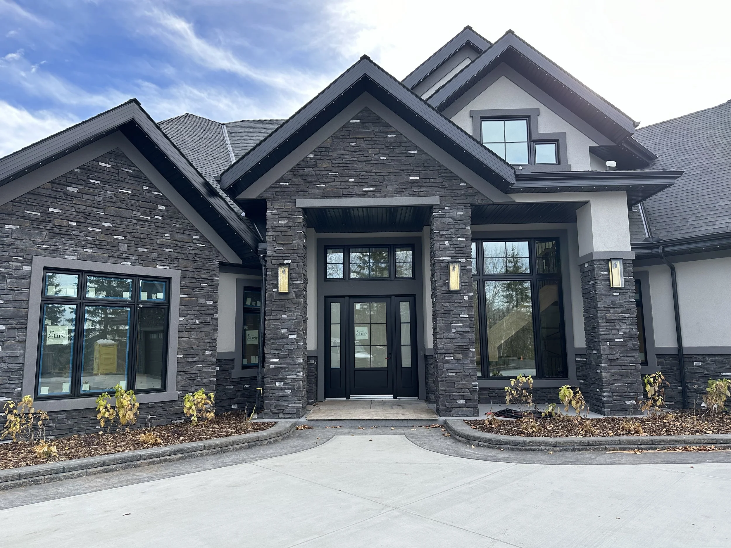 Front view of a modern house with stone and stucco exterior, large windows, and a concrete driveway.