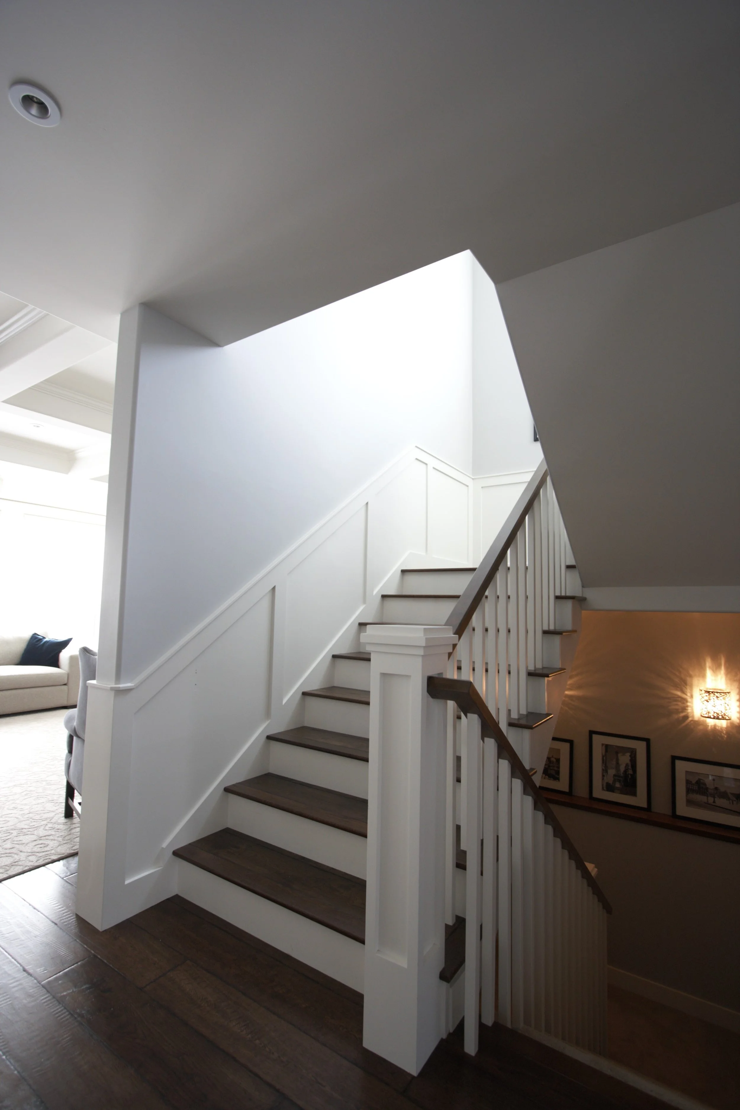 A white staircase with dark wooden steps leading to the upper floor, with a railing on the right and a wall of framed pictures along the stairwell.