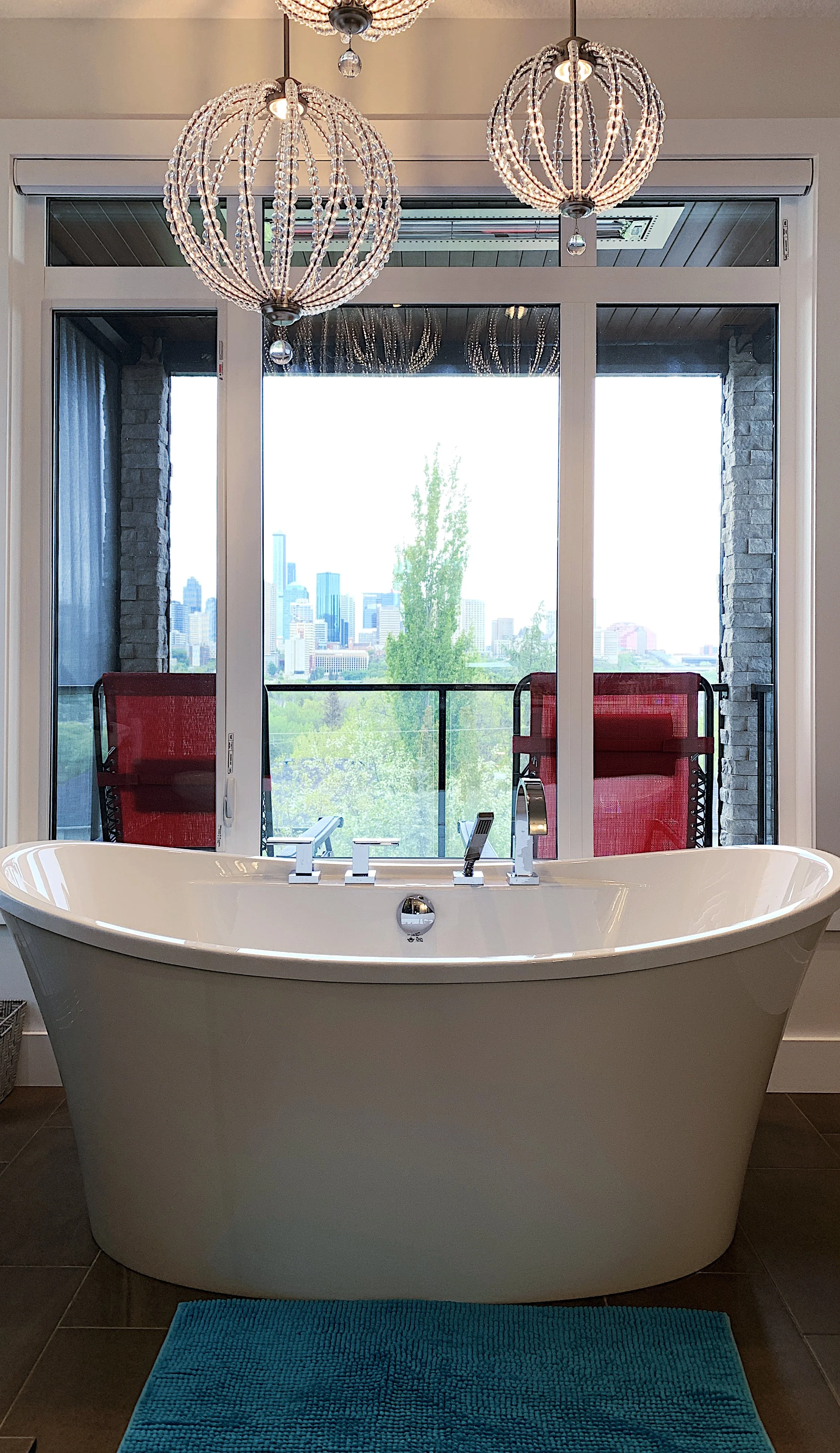 Ensuite bathroom with freestanding tub, floor-to-ceiling windows, pendant lights, and balcony city view