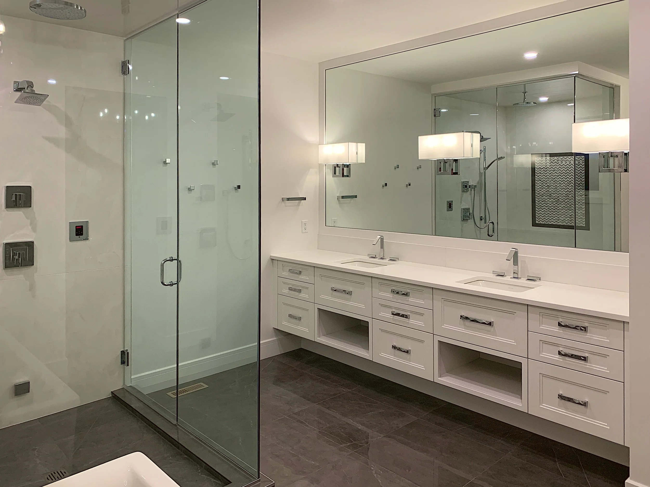 An Ensuite bathroom with white cabinets, double sinks and glass shower