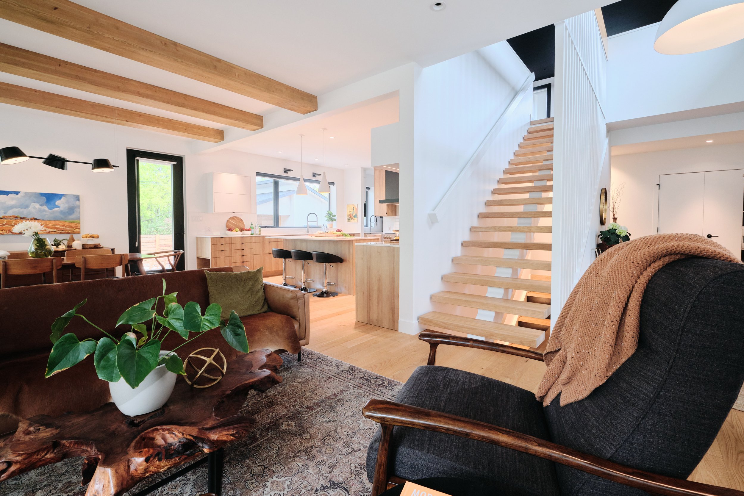 Modern open-concept living area with exposed beams, wood staircase, and custom kitchen in Edmonton.