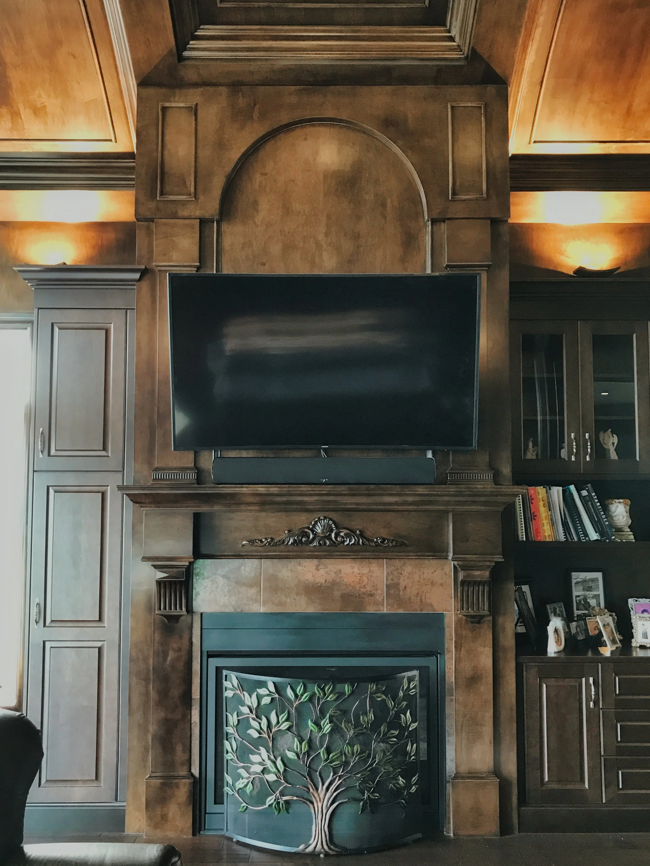 Elegant living room with dark wood fireplace, mounted TV, and upscale built-in cabinetry.