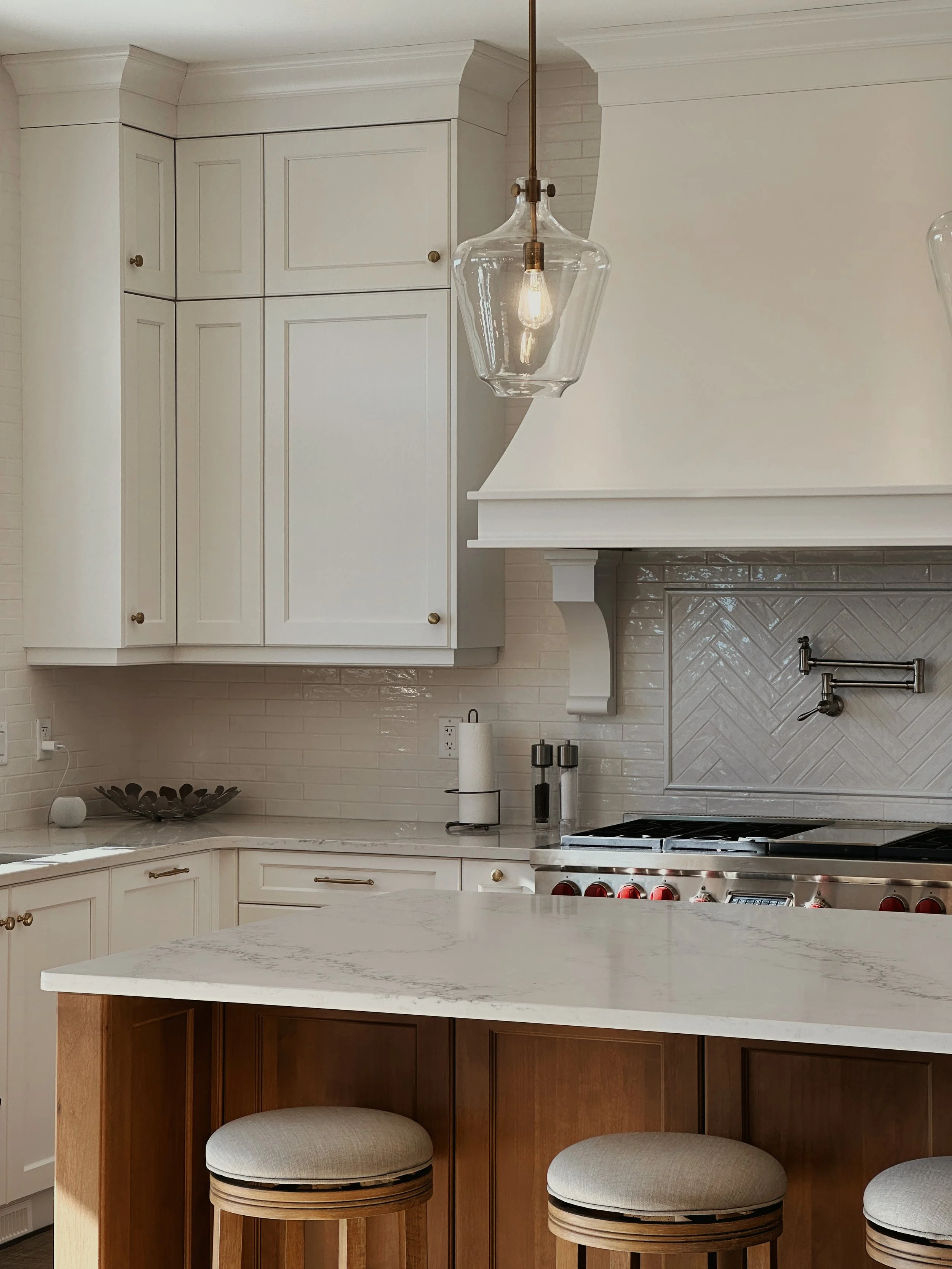A Kitchen with white cabinets, large island and curved rangehood.