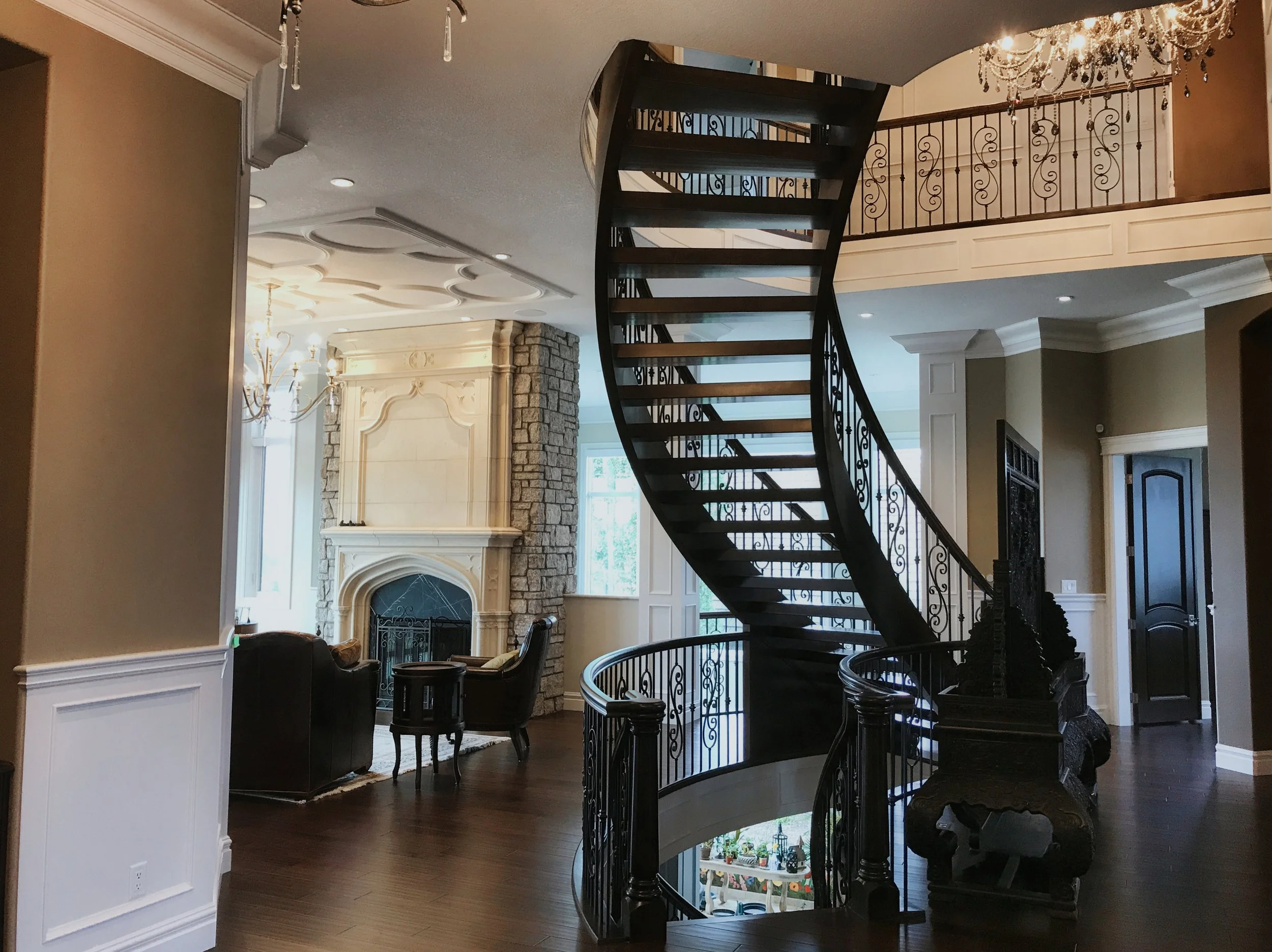 Grand spiral staircase with wrought iron railing and stone fireplace in custom-built Edmonton luxury home.