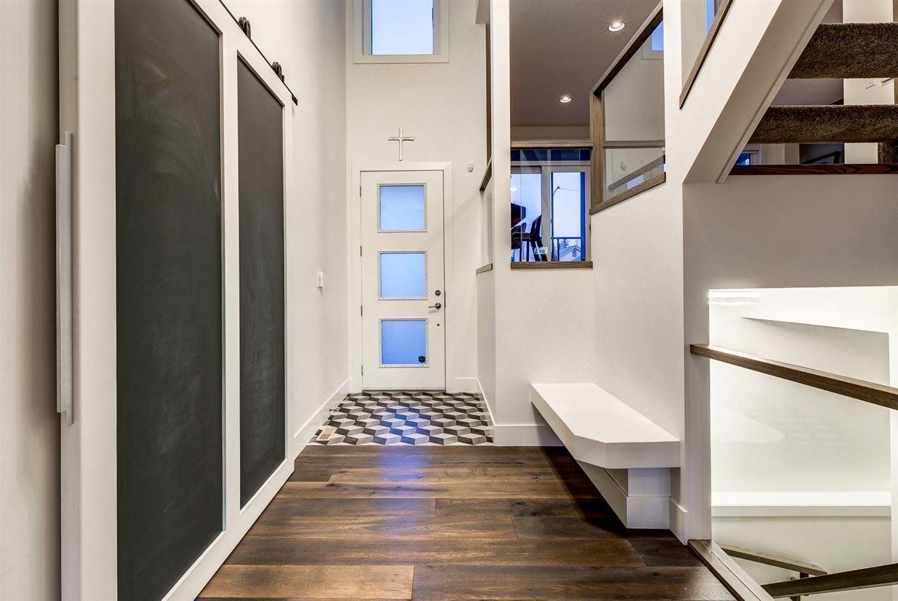 Entryway with black and white patterned tile floor, white door with glass panes, staircase with wooden steps, and on the wall to the left, two black chalkboard barn doors framed in white.