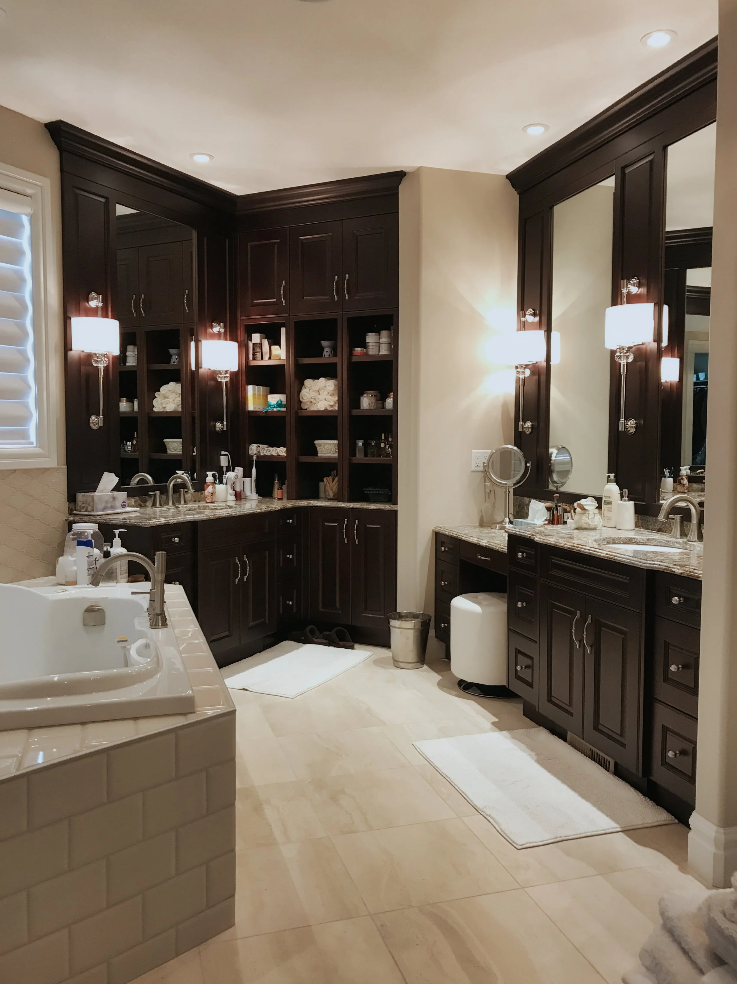 Well-appointed bathroom featuring organized shelving, granite sinks, and a spacious tiled bathtub.