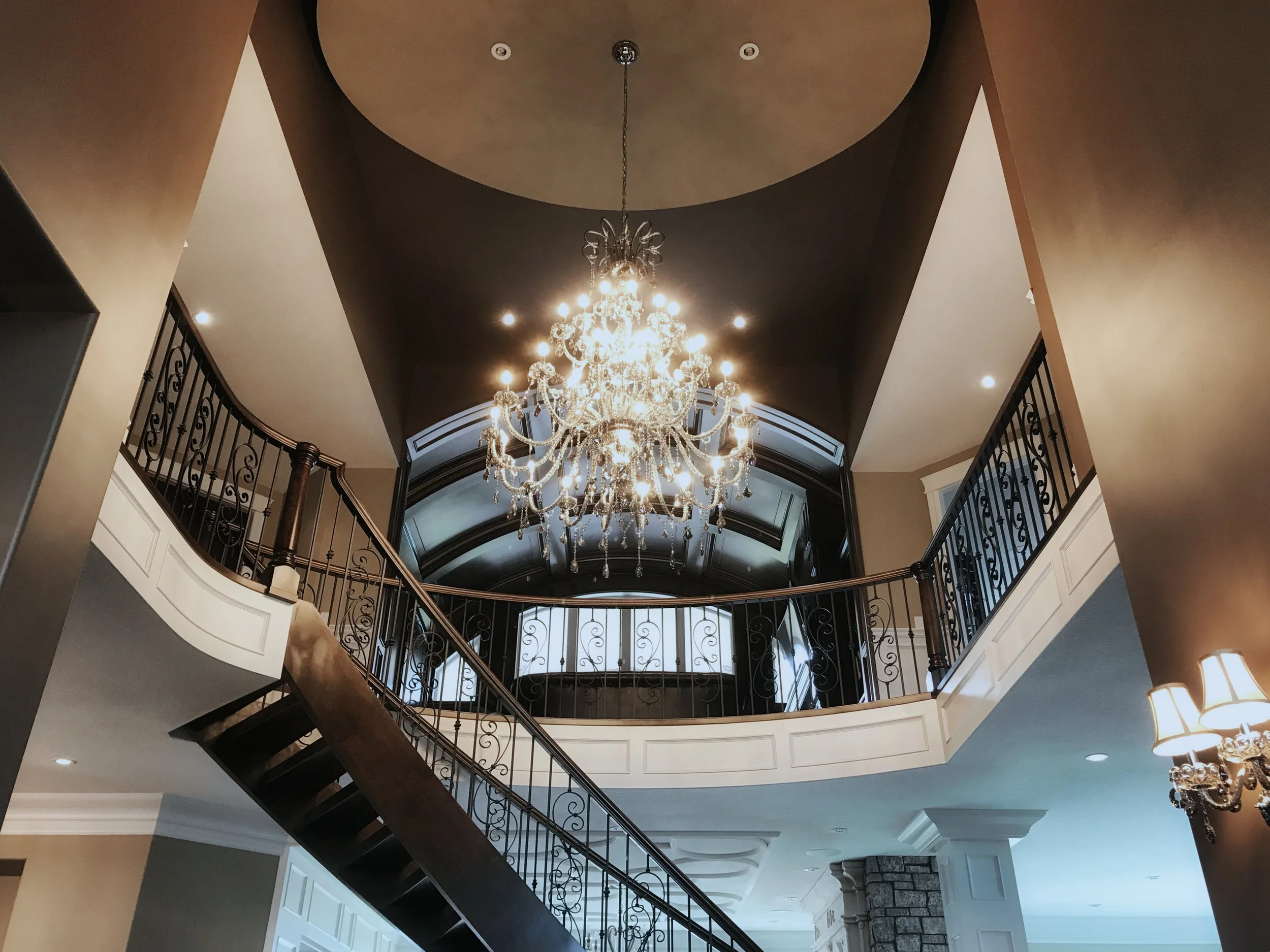 Luxurious custom home interior with grand curved staircase, crystal chandelier, and elegant architectural details