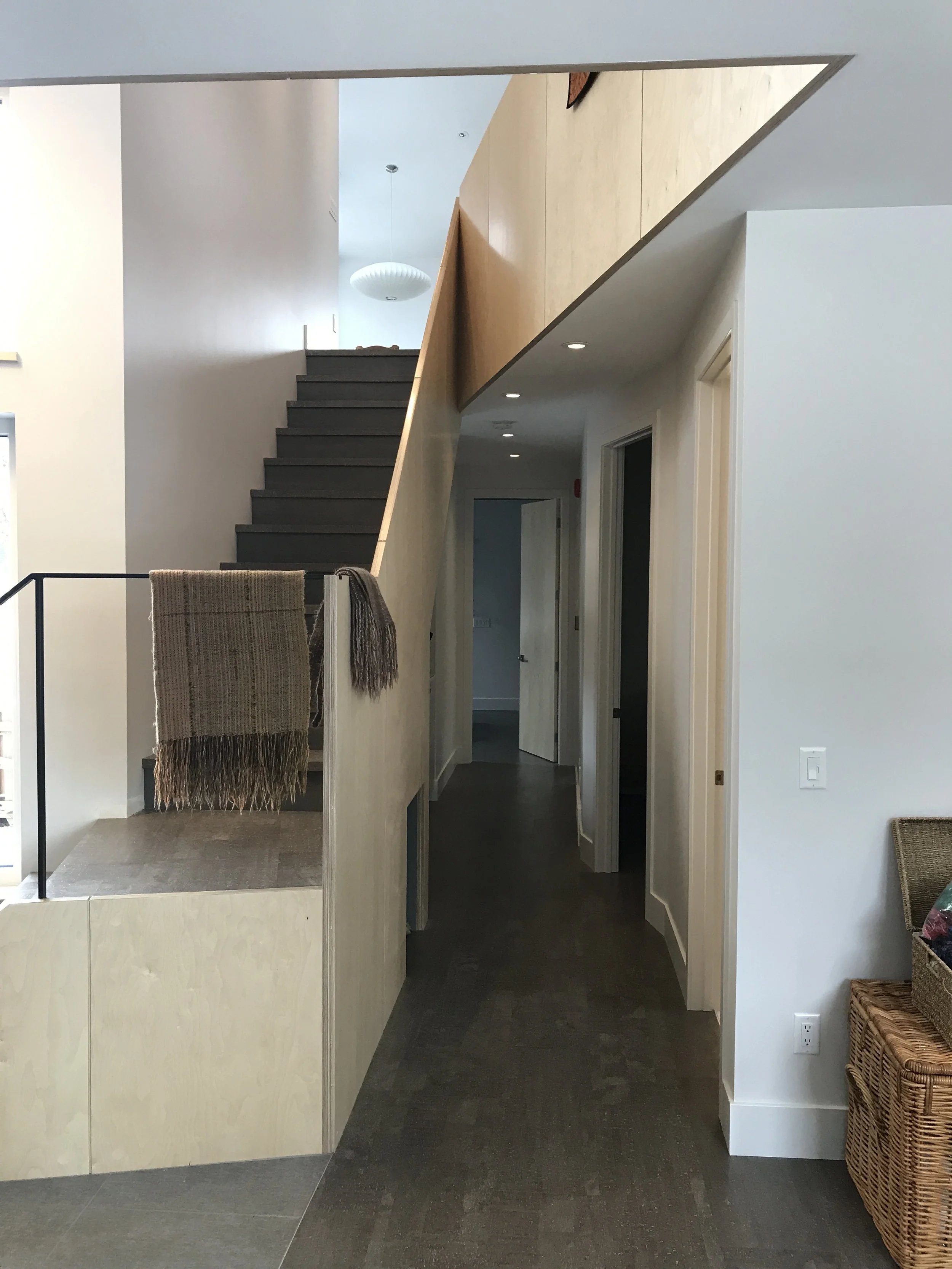 Modern hallway interior with dark flooring, white walls, wood-paneled ceiling, staircase, woven decor, and wicker accents—minimalist design blending natural textures with contemporary architecture.
