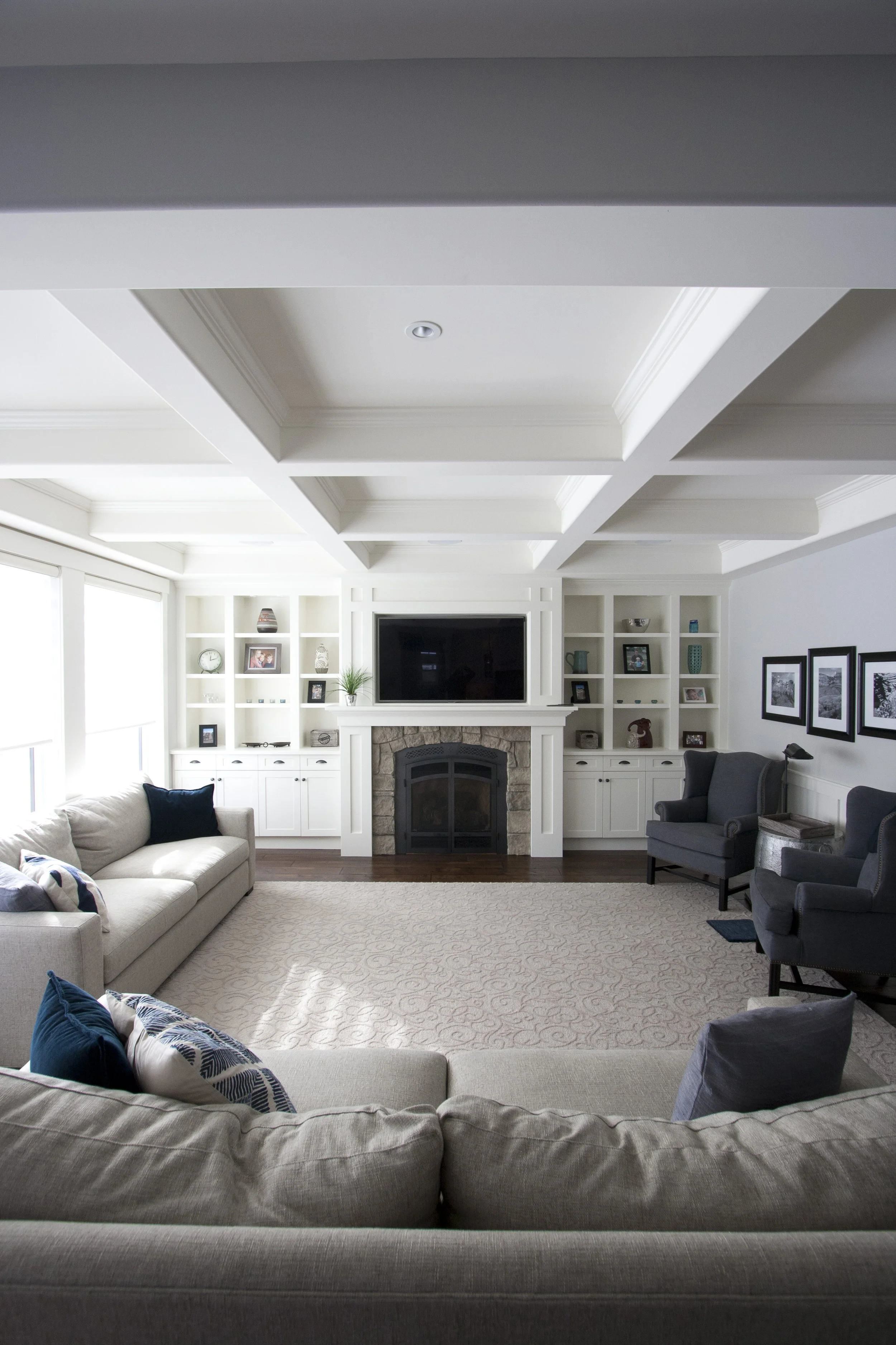 A living room with coffered ceiling and fireplace with custom cabinets