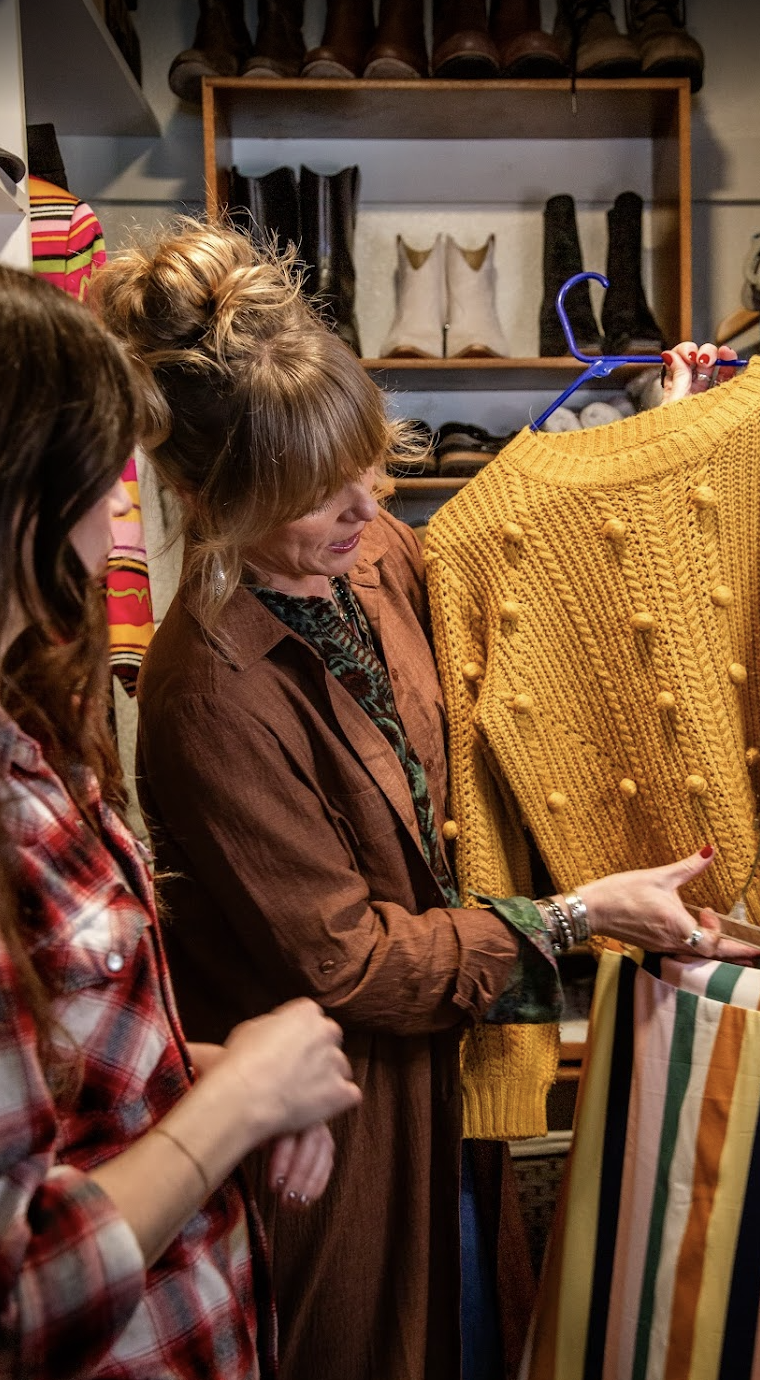 Women shopping for a bright yellow knitted sweater with pom-poms in a clothing store.