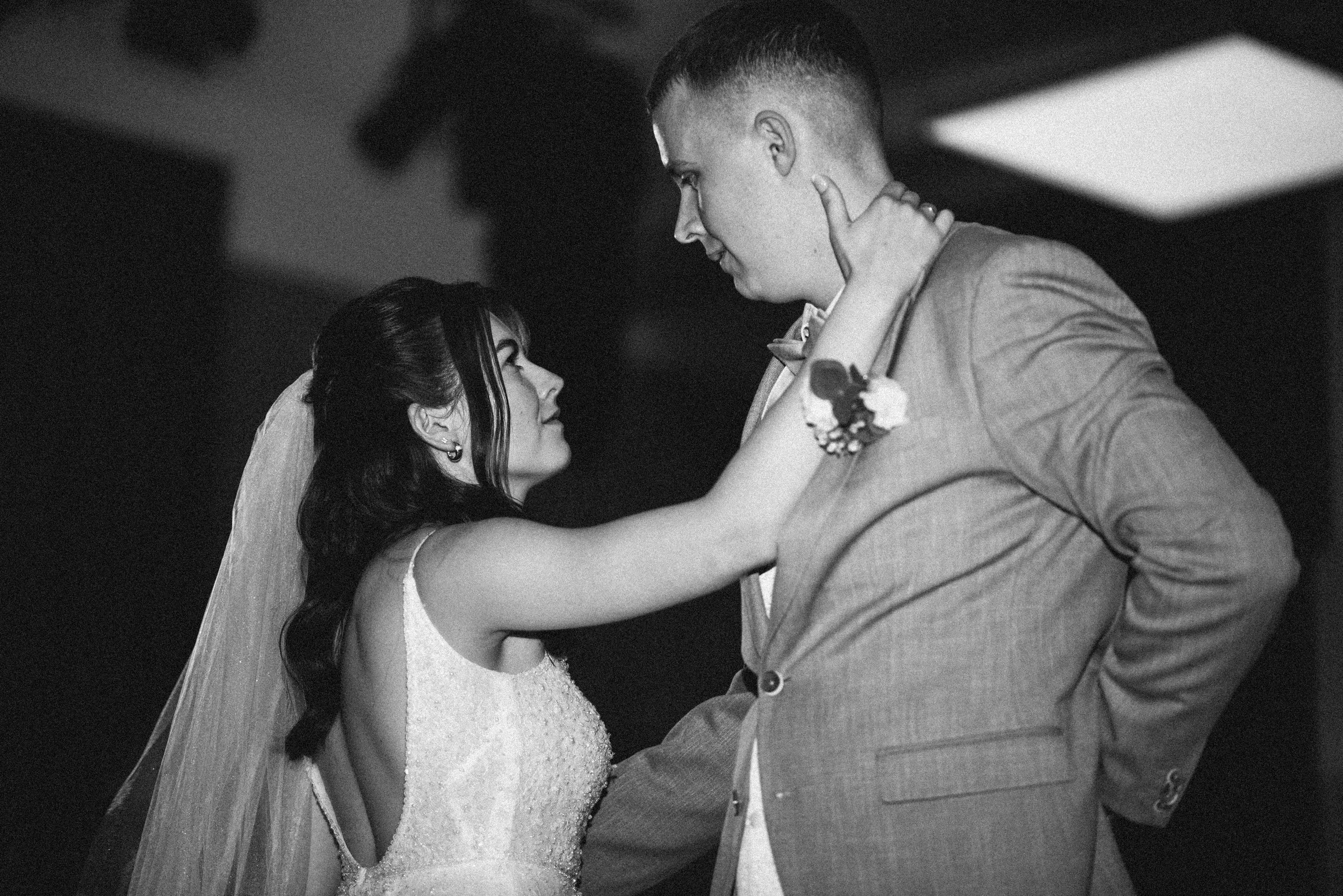 A black and white photo of a bride and groom dancing closely, gazing at each other, with the bride holding the groom's neck and the groom resting his hand on his hip.