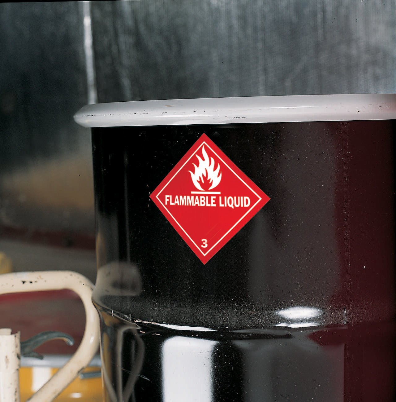 A black container with a red diamond-shaped label that reads "Flammable Liquid" and has a flame symbol on it.