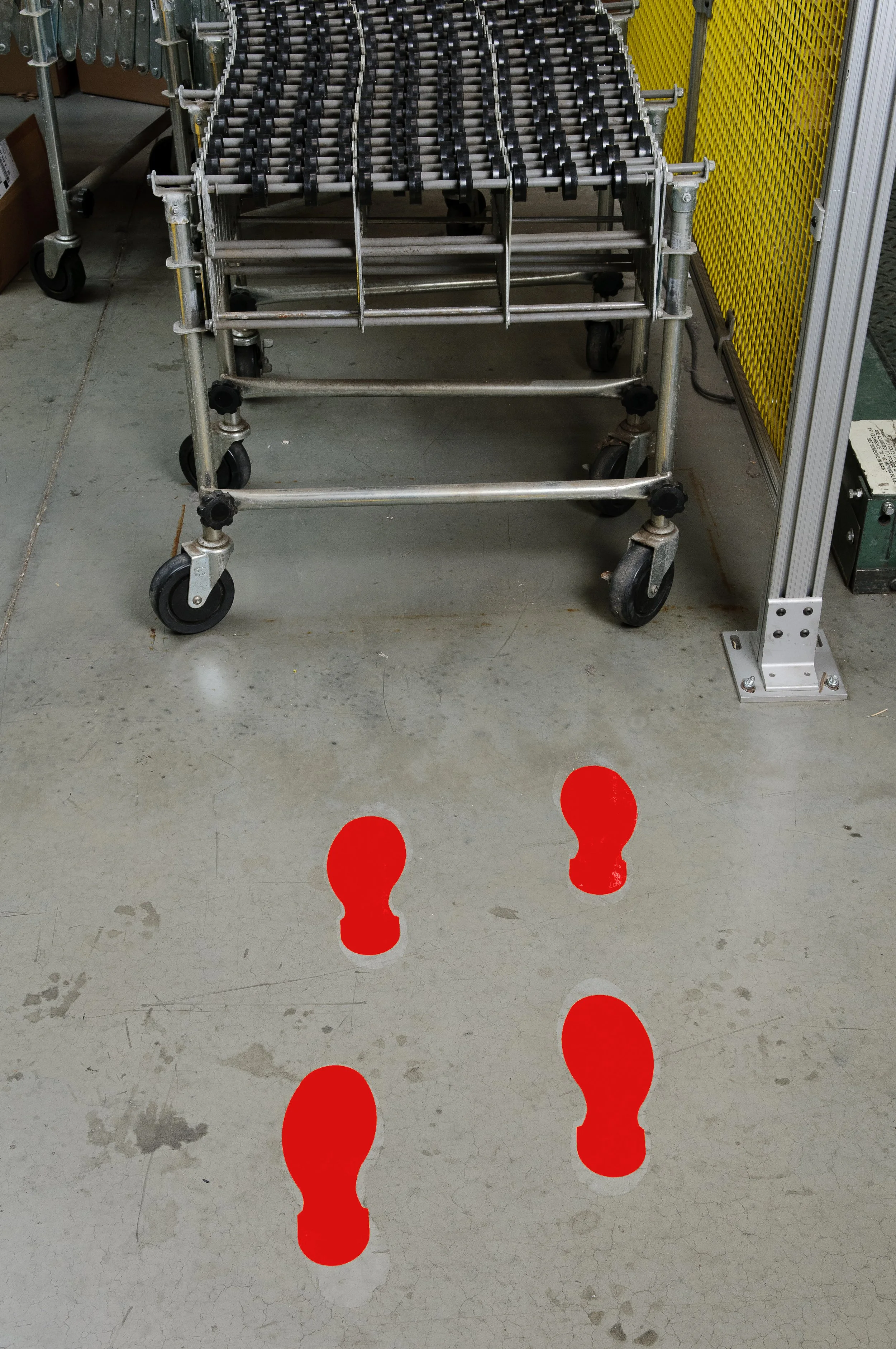 Industrial work area with a rolling metal cart and red footprint markers on the concrete floor.