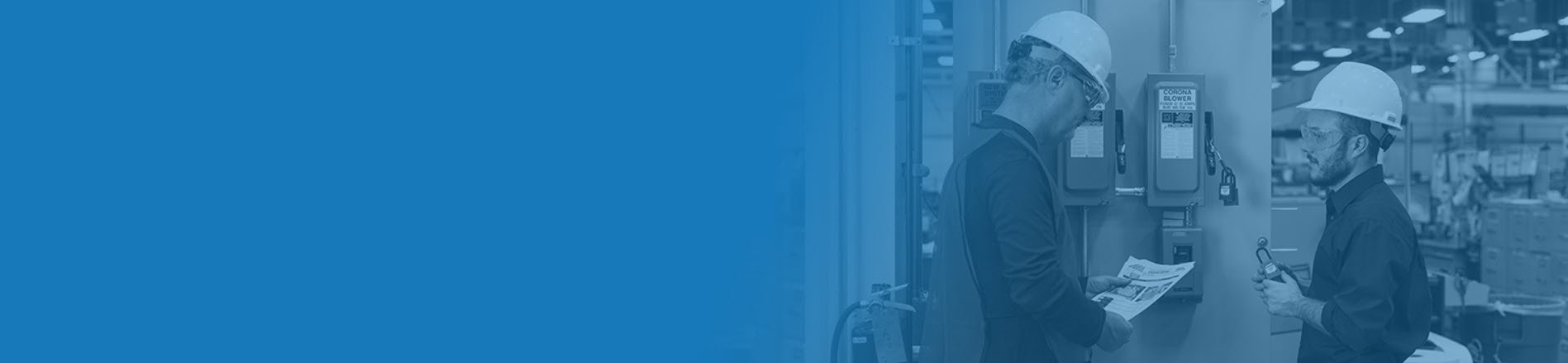 Two workers wearing safety helmets and glasses inspecting industrial equipment in a factory.