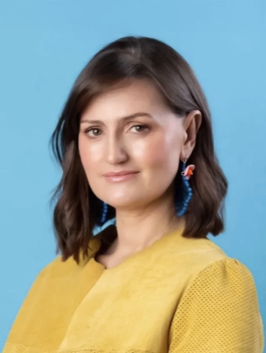 Woman in yellow top with blue earrings against a blue background