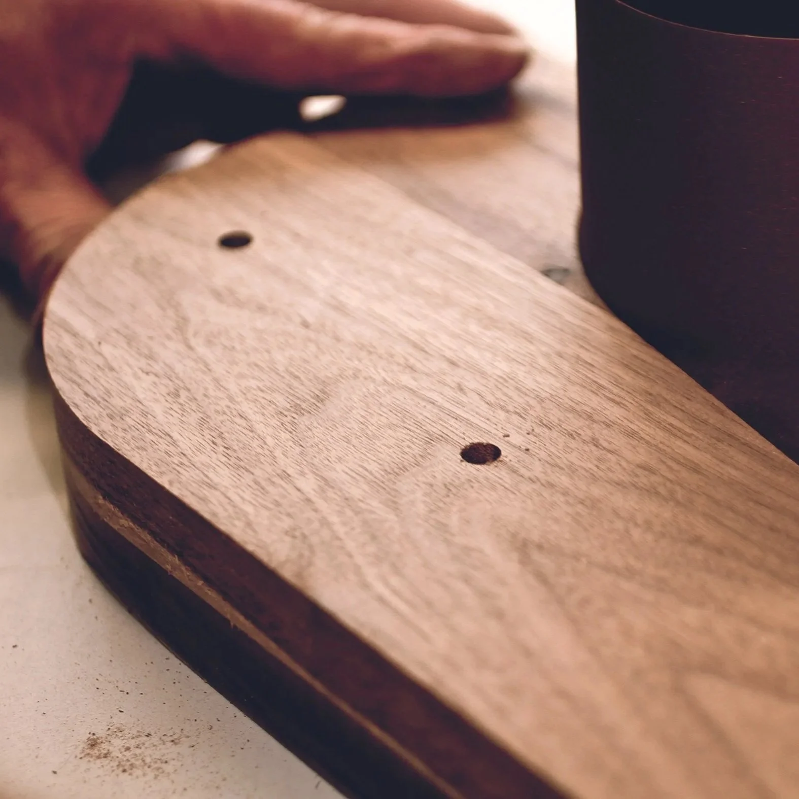 Close-up of a person holding a piece of wood, with a dark-colored mug on the surface.
