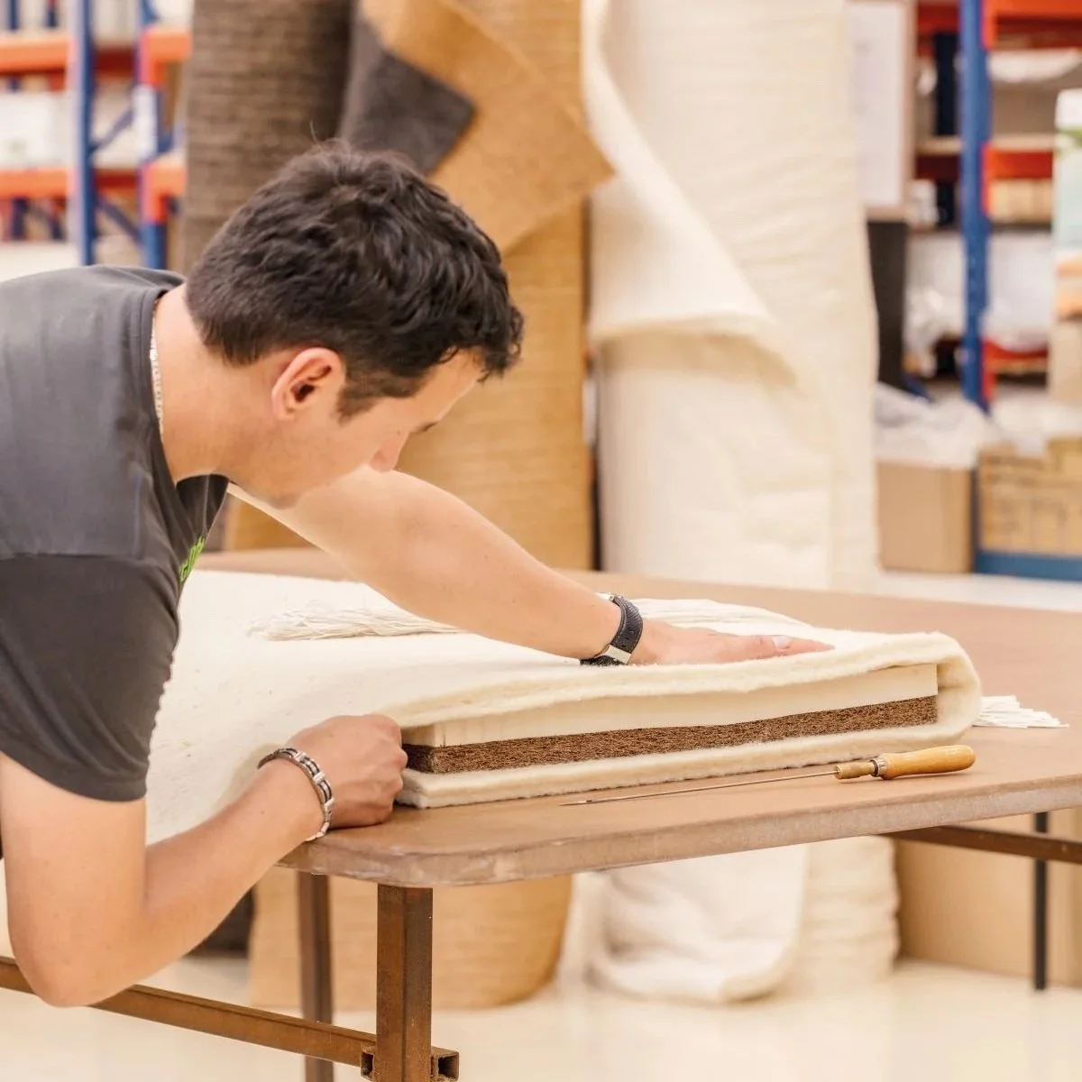 A man working on a piece of furniture, using a tool to craft or upholster a padded surface with fabric in a workshop.
