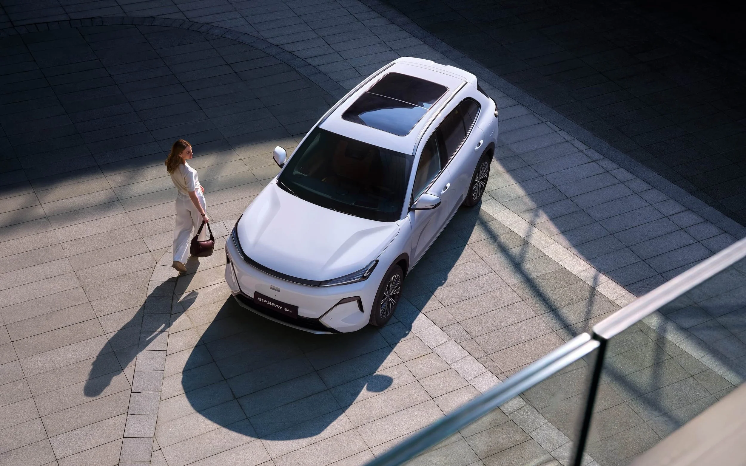 Mujer con bolso junto a coche blanco en una ciudad moderna durante el día.