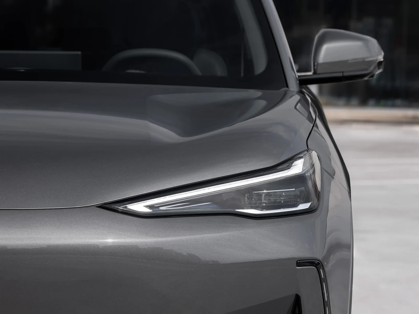 Primer plano del lado delantero de un auto gris con enfoque en la farola y el espejo lateral.