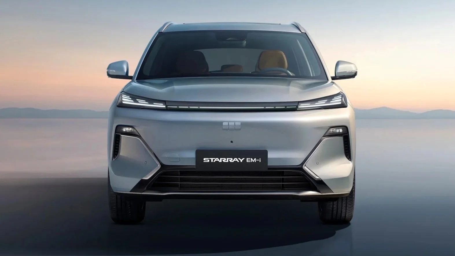 Frontal de un coche eléctrico desde el frente, modelo Starry EM-i, con fondo de paisaje con montañas y cielo al atardecer.