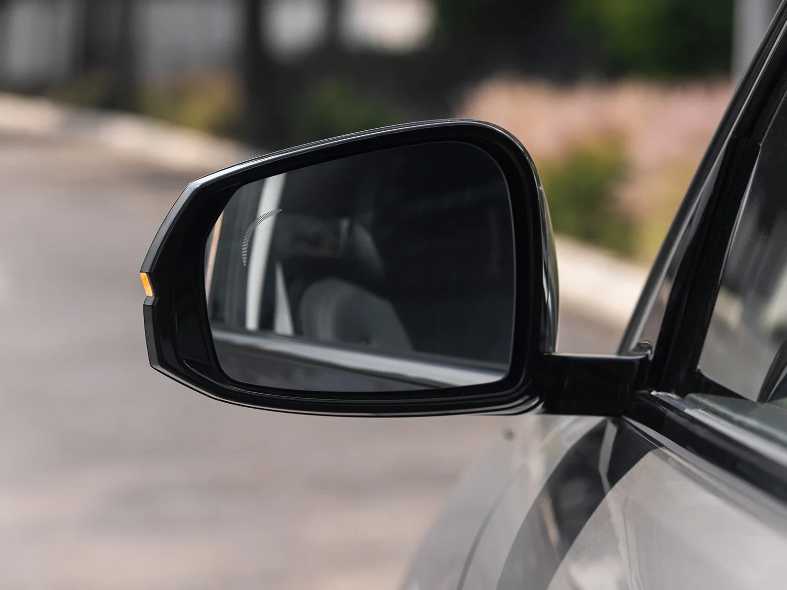 Espejo lateral de un coche con fondo borroso de una calle y vegetación