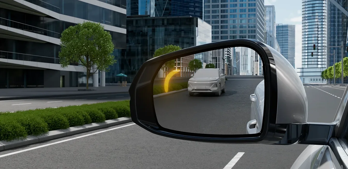 Vista desde el espejo retrovisor de un automóvil mostrando otros coches en una calle rodeada de edificios altos y árboles.