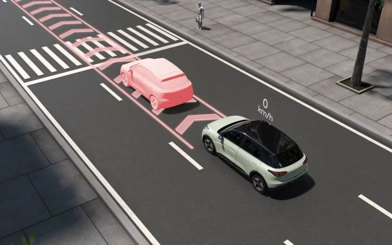 Una imagen que muestra la carretera con marcas de advertencia para peatones, una señal de velocidad máxima y un vehículo en modo de conducción autónoma con detección de peatones, y otras marcas viales y semáforo.