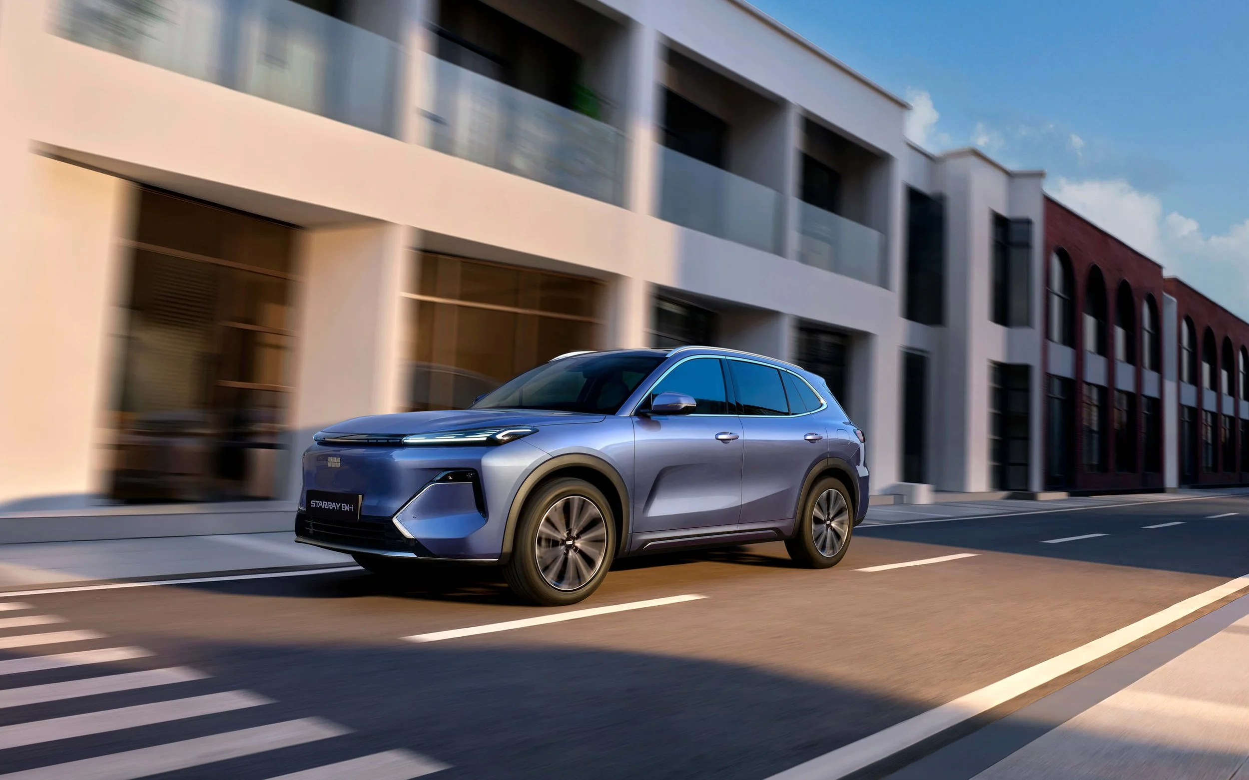 Un coche azul moderno conduciendo por una calle urbana con edificios en el fondo y un cielo despejado.