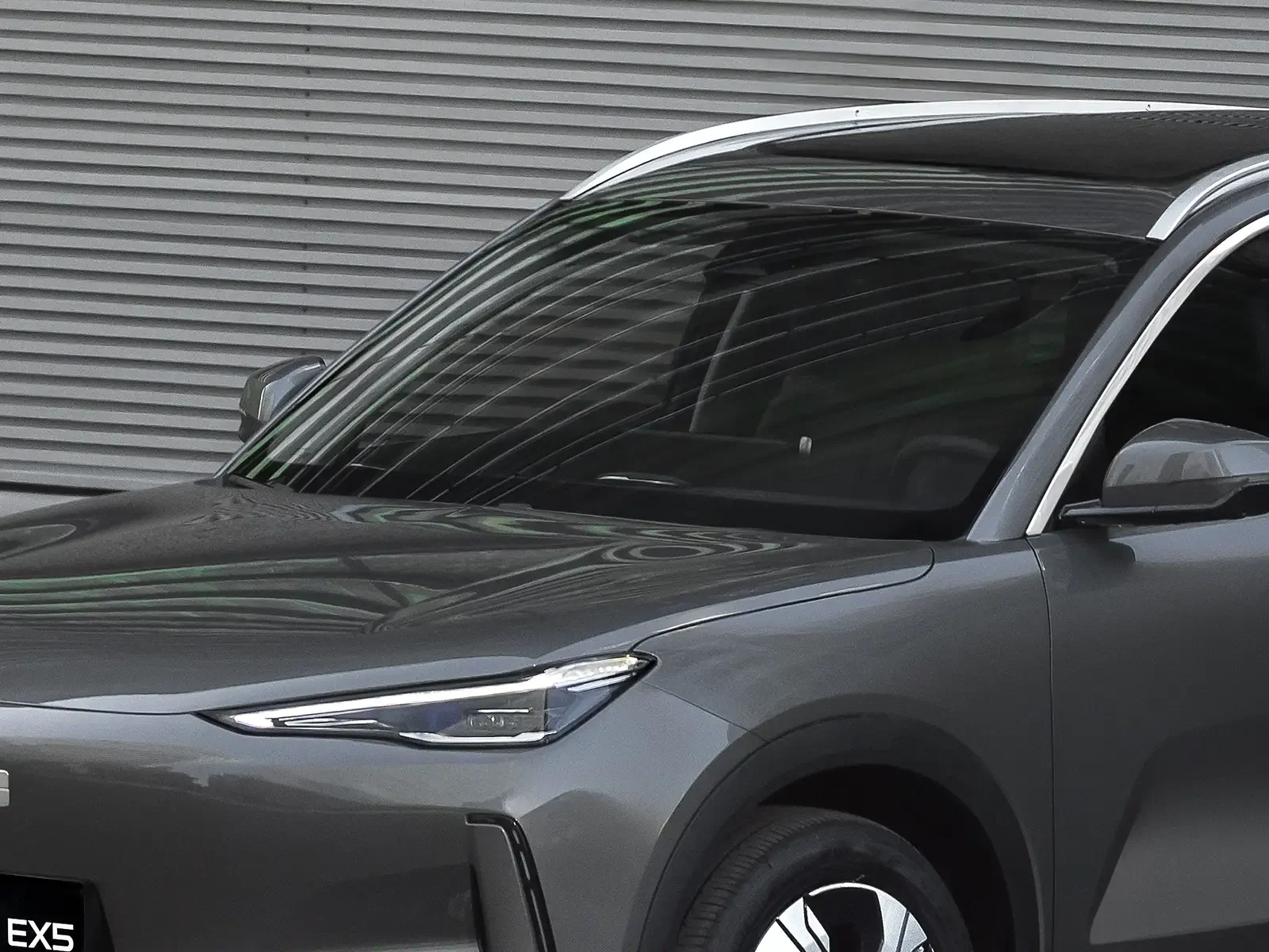 Coche SUV gris estacionado frente a una pared de metal horizontal.