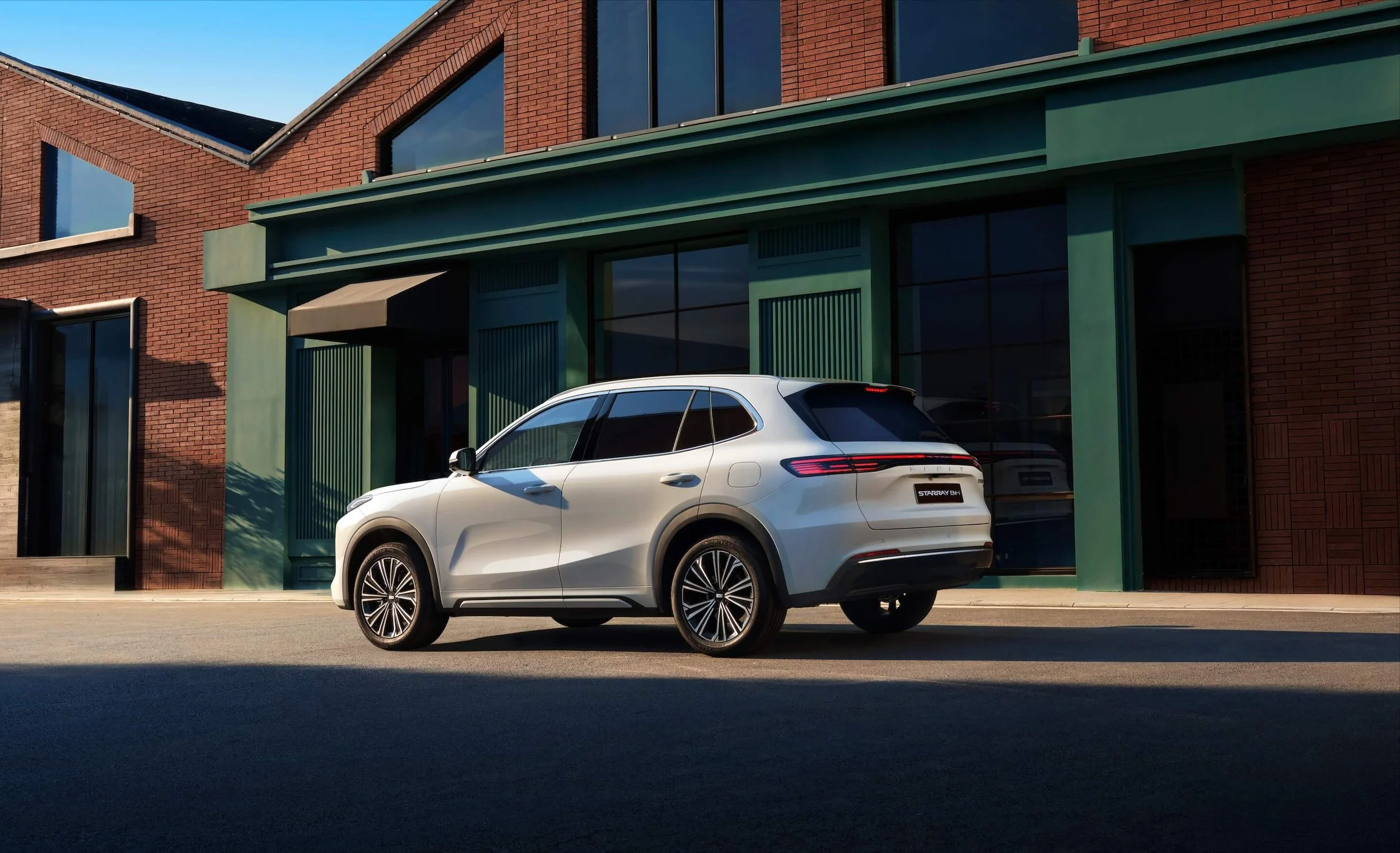 Auto SUV blanco estacionado frente a un edificio de ladrillos y ventanas grandes en un día soleado.
