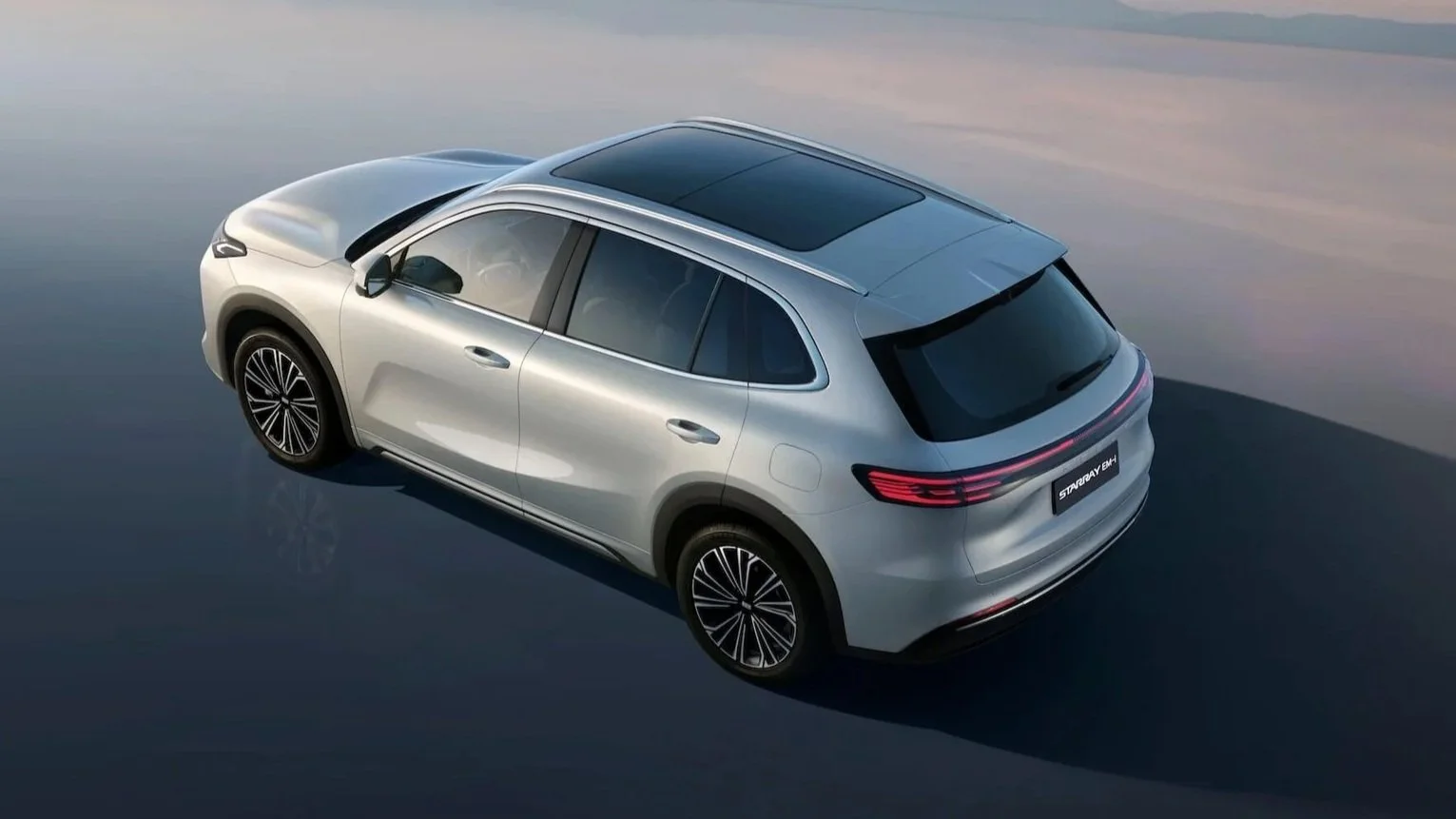 Coche SUV plateado en una superficie reflectante con cielo claro al fondo.