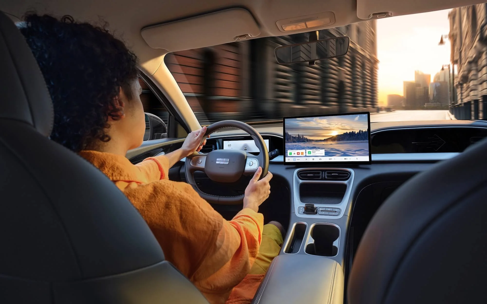 Conductor en un coche, mirando la calle a través del parabrisas, con un monitor digital en el tablero mostrando un paisaje y el atardecer.