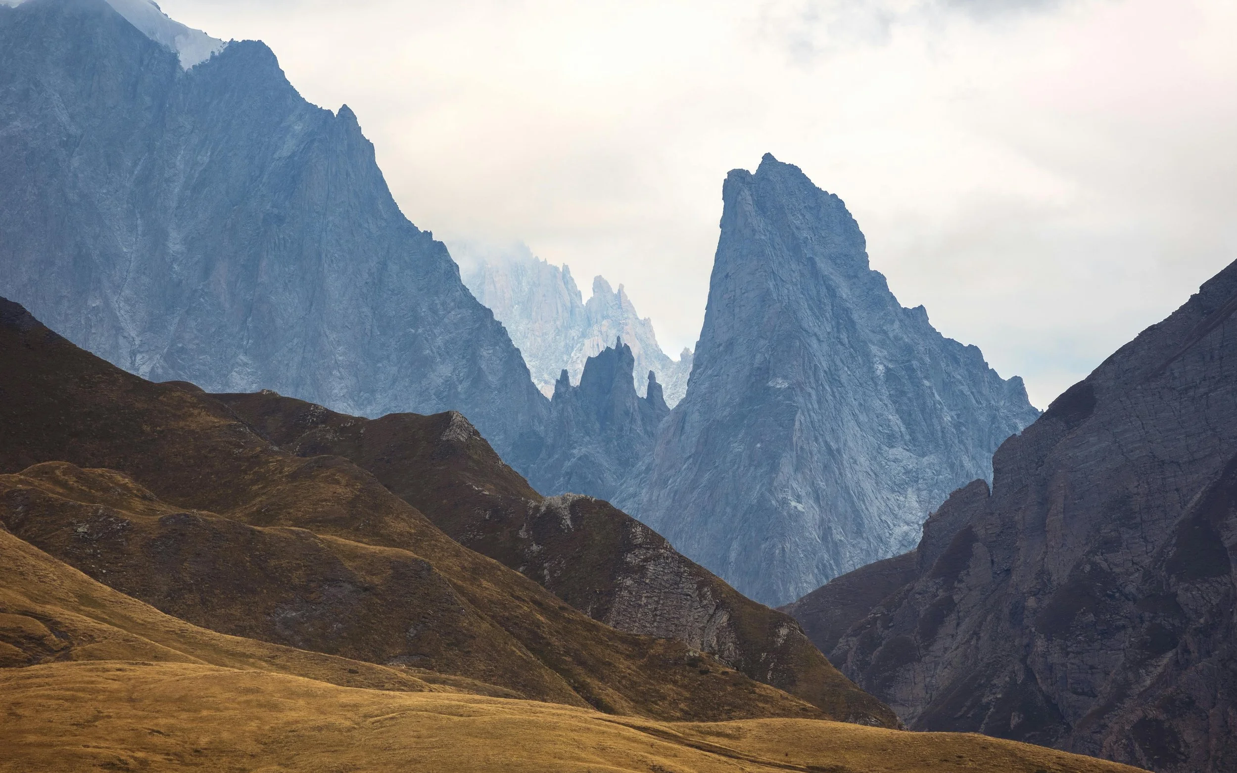 Mountain landscape with rugged peaks and rolling grassy hills in the foreground.