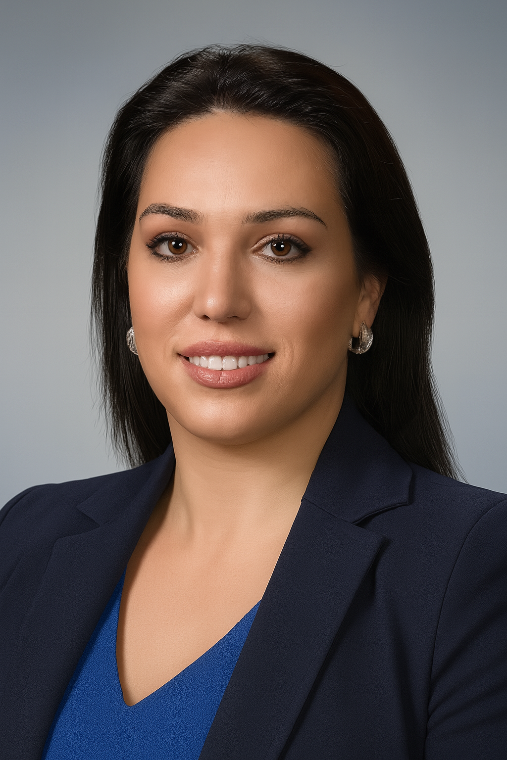 Professional woman with dark hair, wearing a dark blazer and blue top, smiling against a plain gray background.