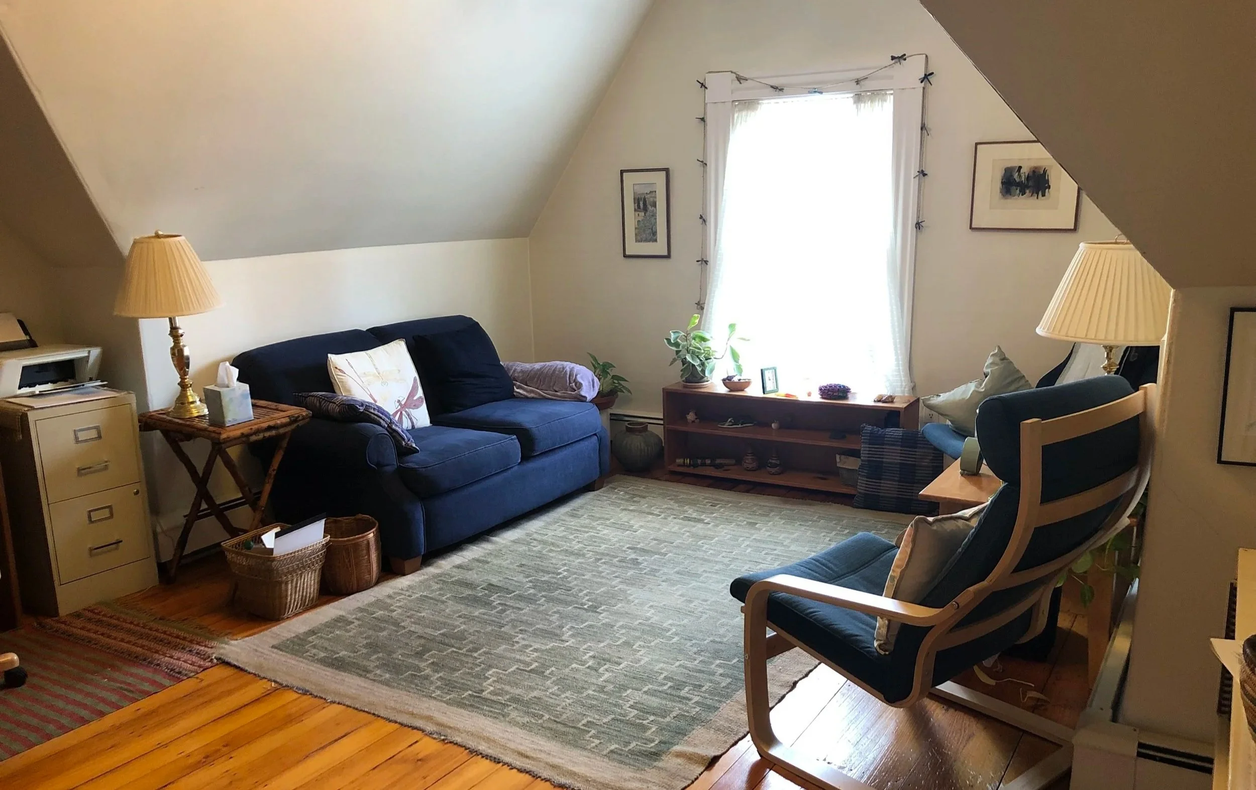 Cozy living room with a sloped ceiling, blue sofa, armchair, curtains, and wooden furniture.