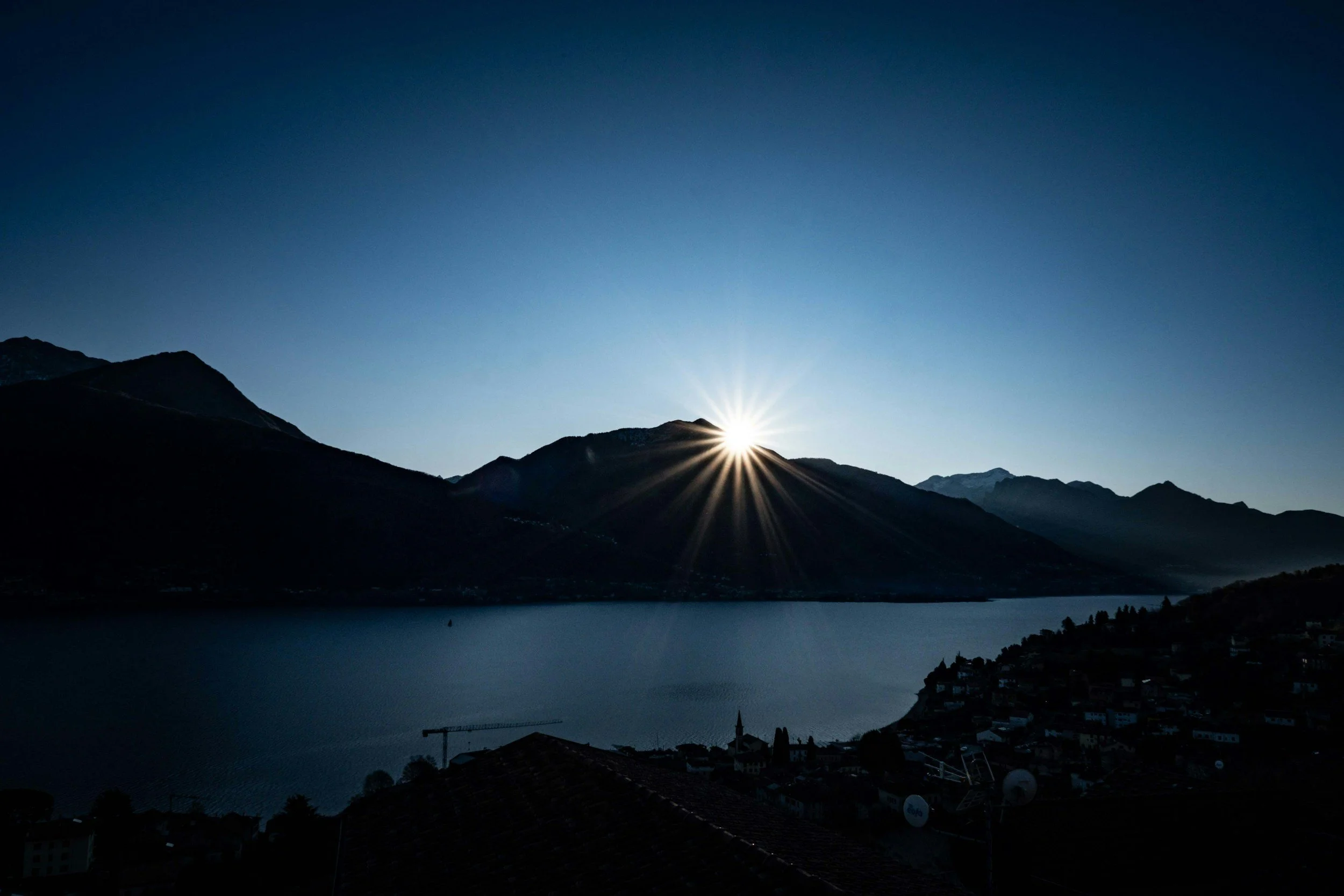 Sunset over a mountain lake with the sun setting behind mountains, creating a starburst effect