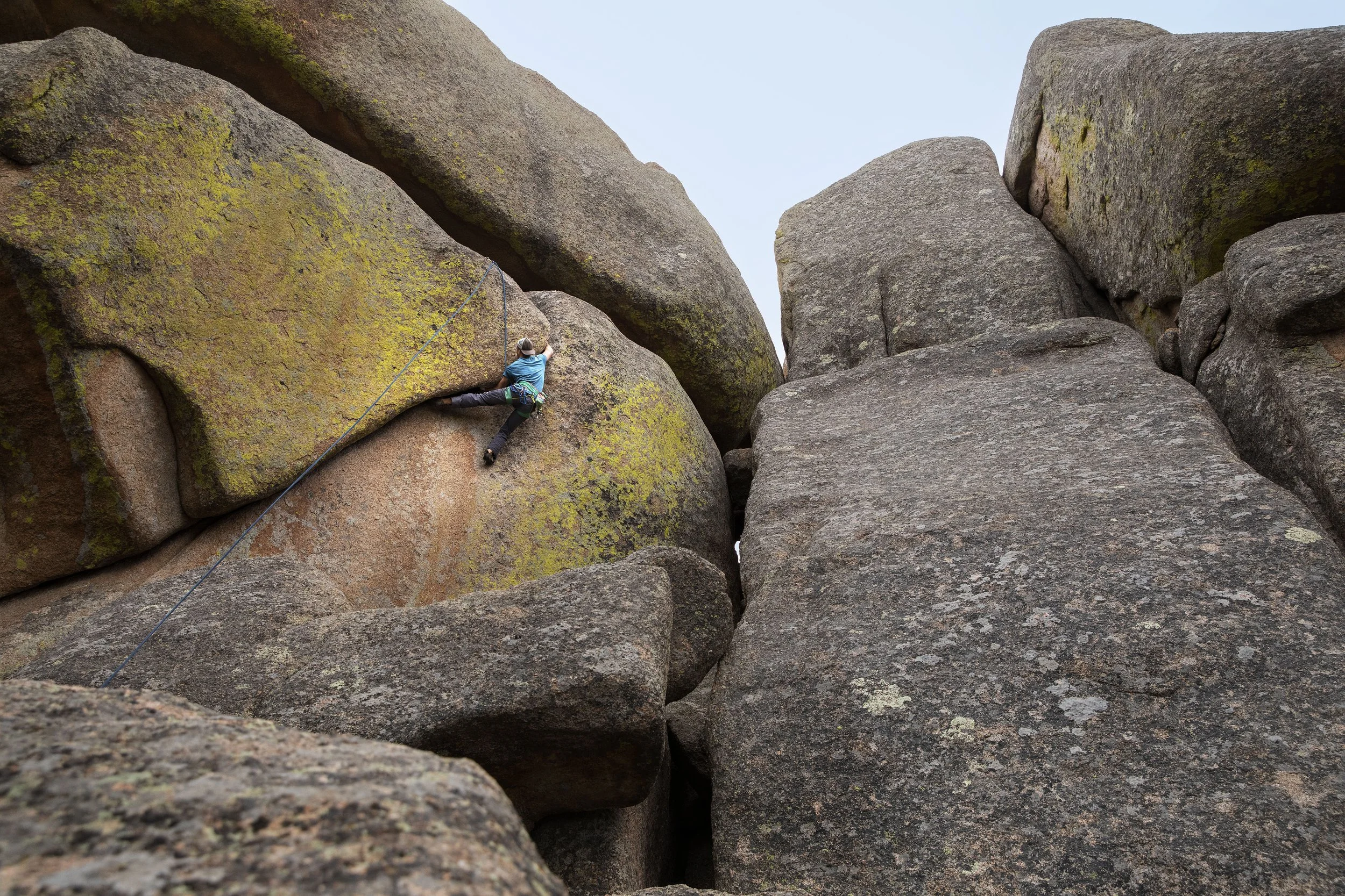 A person climbing large rocks outdoors, using a climbing harness and rope for safety.