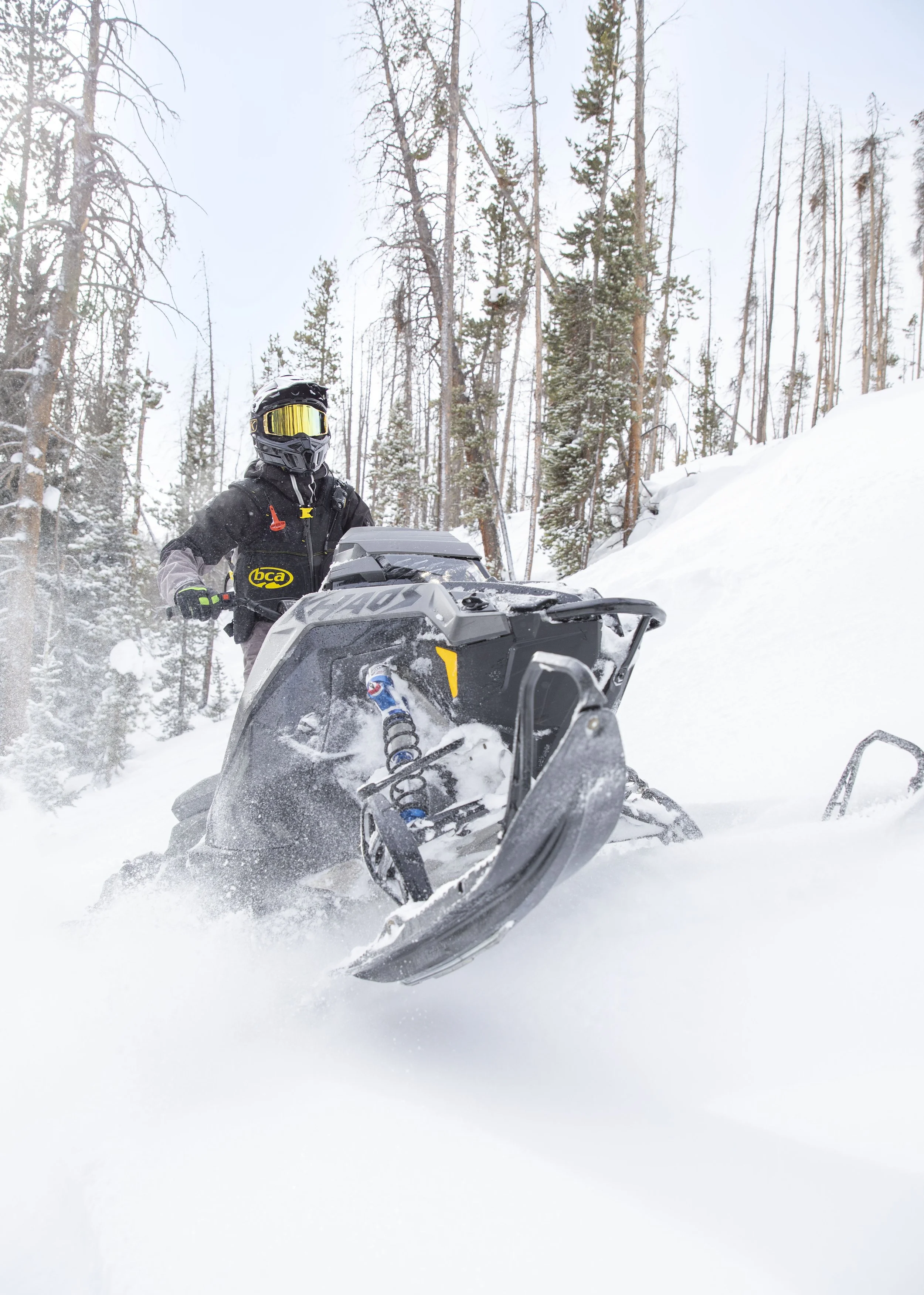 Person in snow gear riding a snowmobile through snowy forest landscape.