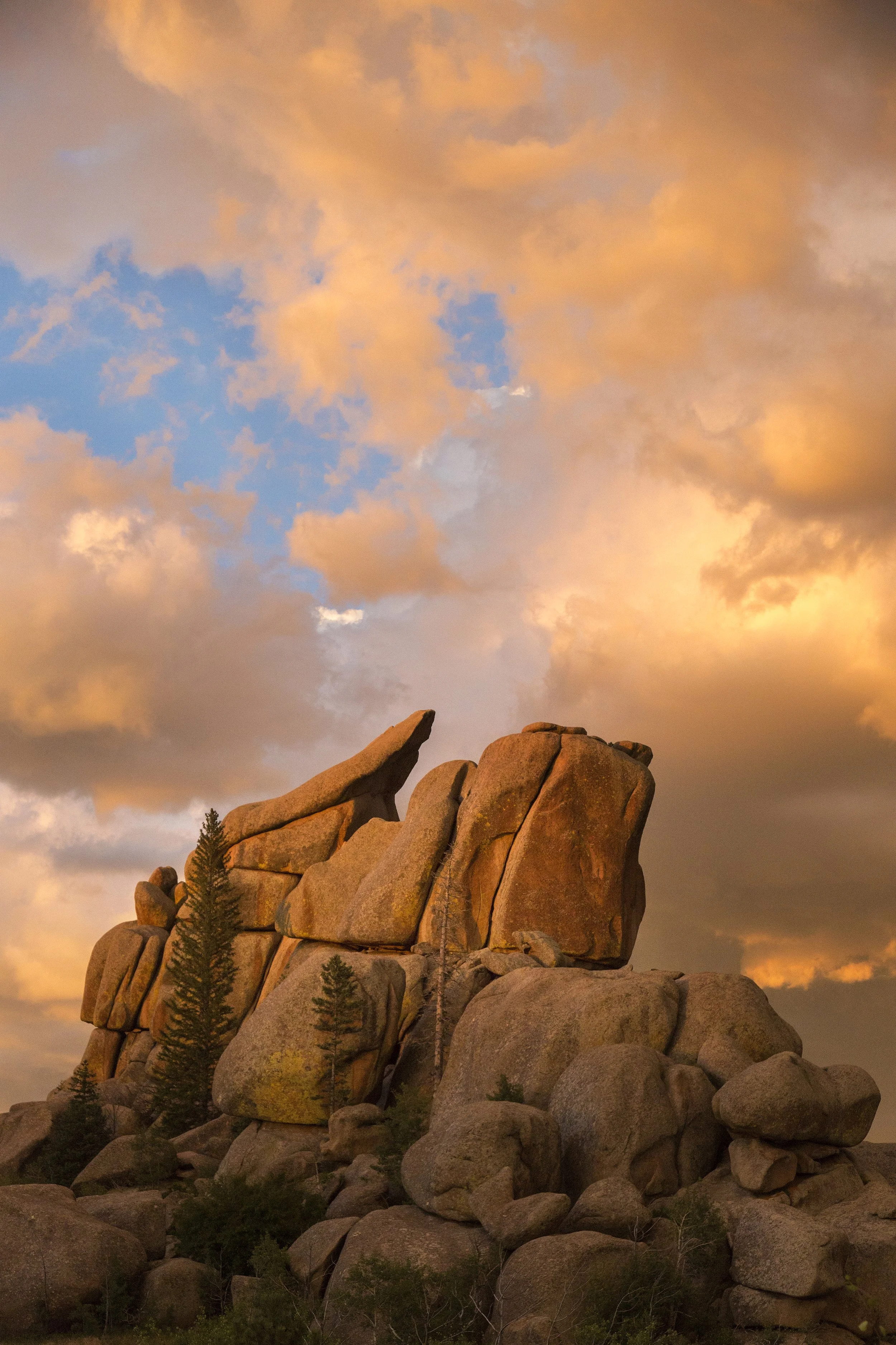 Large rock formations and trees under a dramatic orange and pink sunset sky.